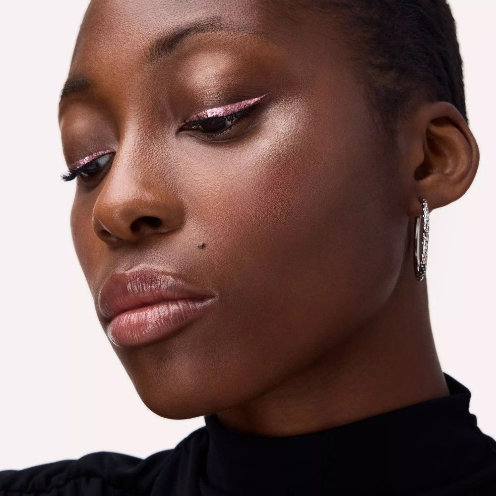 Nahaufnahme eines Gesichts. Rosa Eyeliner auf dem oberen Augenlid. Person mit dunkler Hautfarbe.