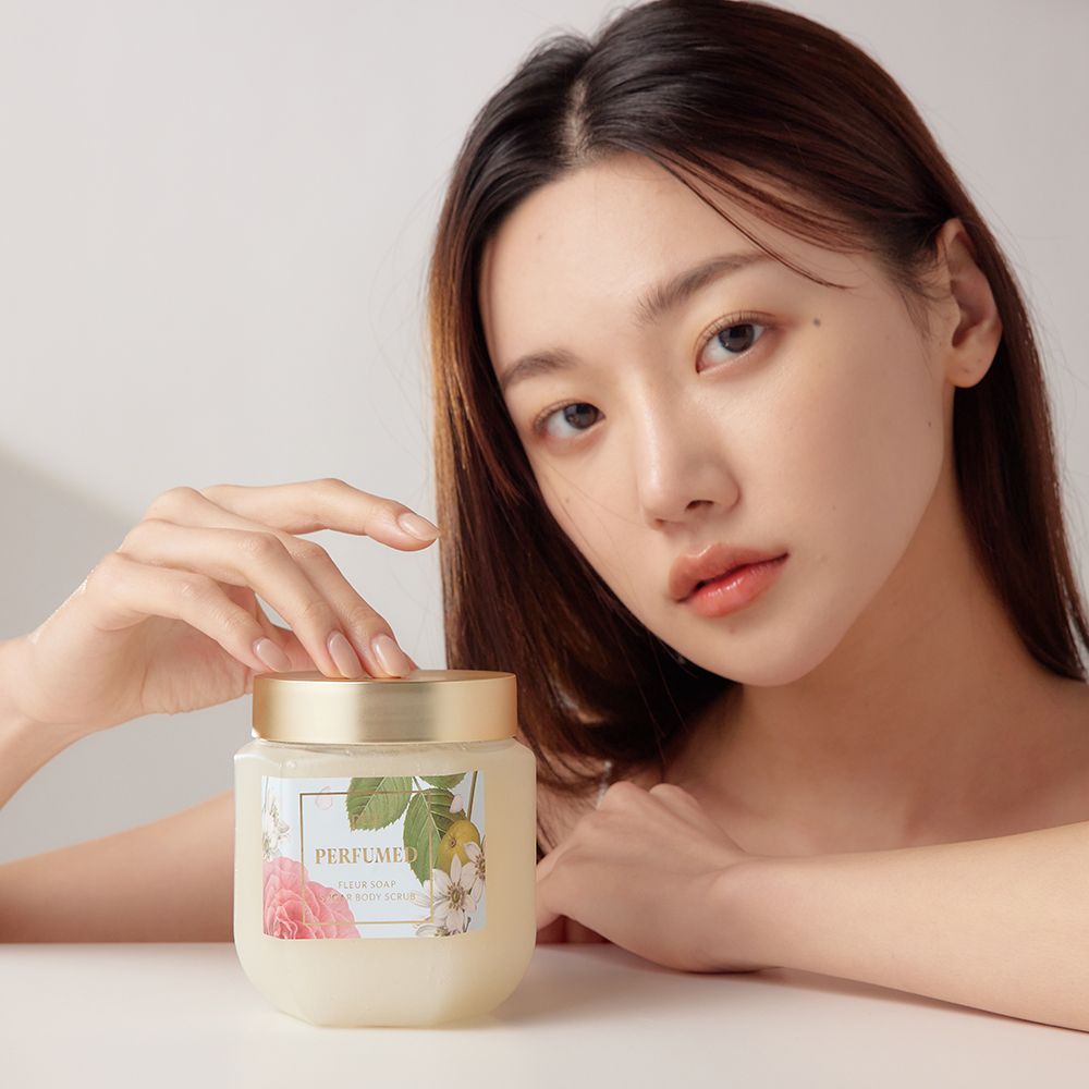 Person hält Glasbehälter mit goldfarbenem Deckel. Aufschrift: PERFUMED FLEUR SOAP SUGAR BODY SCRUB.
