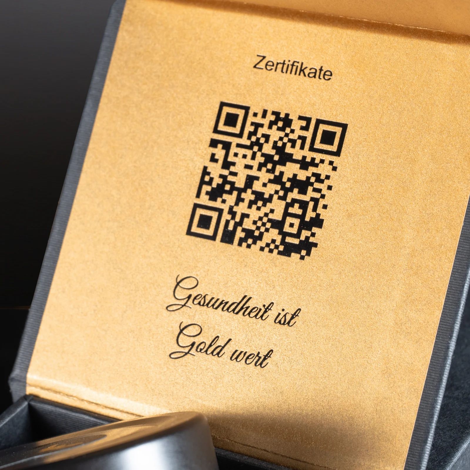Nahaufnahme der Innenseite einer Geschenkbox. QR-Code, Text: Gesundheit ist Gold wert. Schriftzug: Zertifikate.