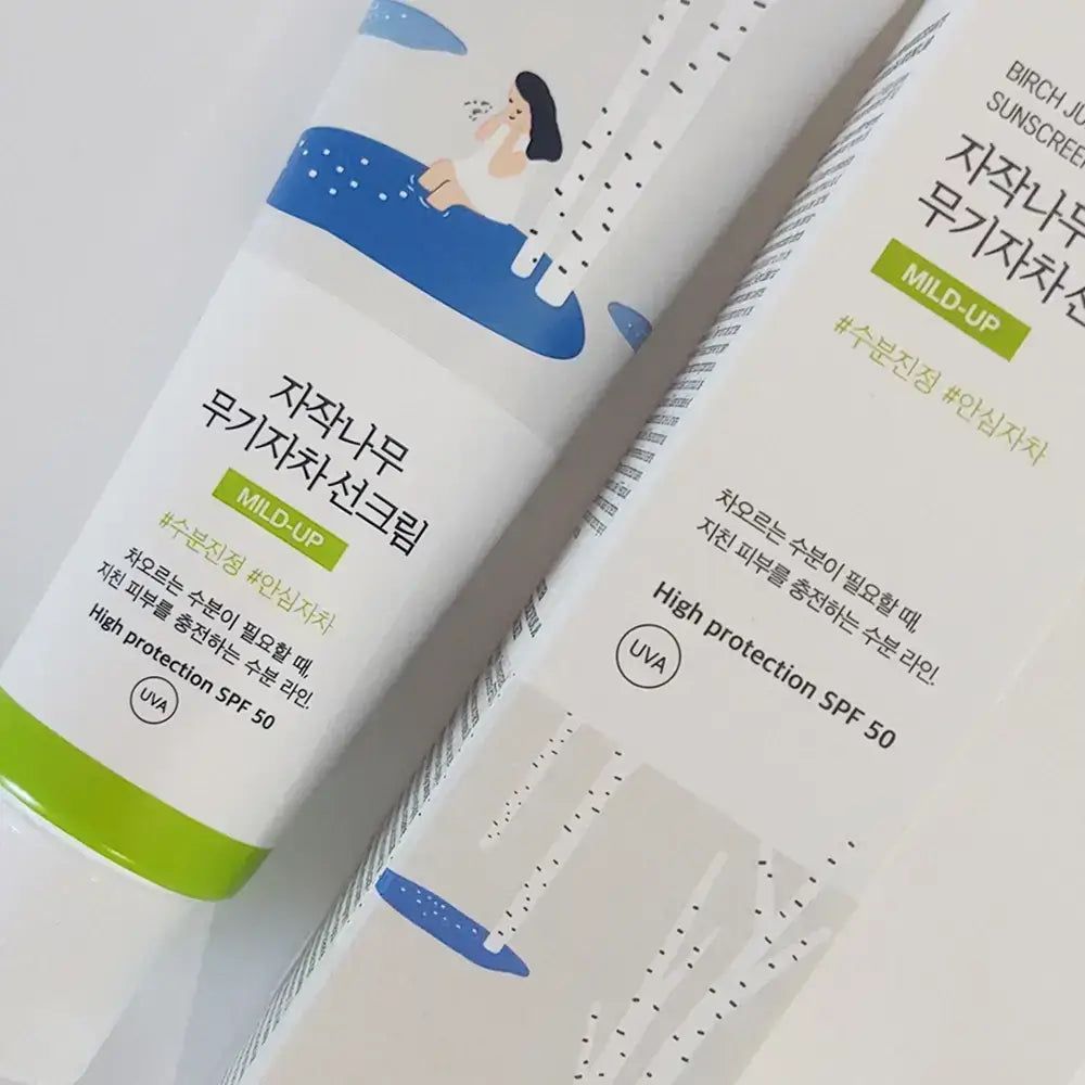 Zwei Tuben Sonnenschutzmittel. Weiß, grüne Akzente. Text in koreanischer Sprache und "MILD-UP SPF 50".