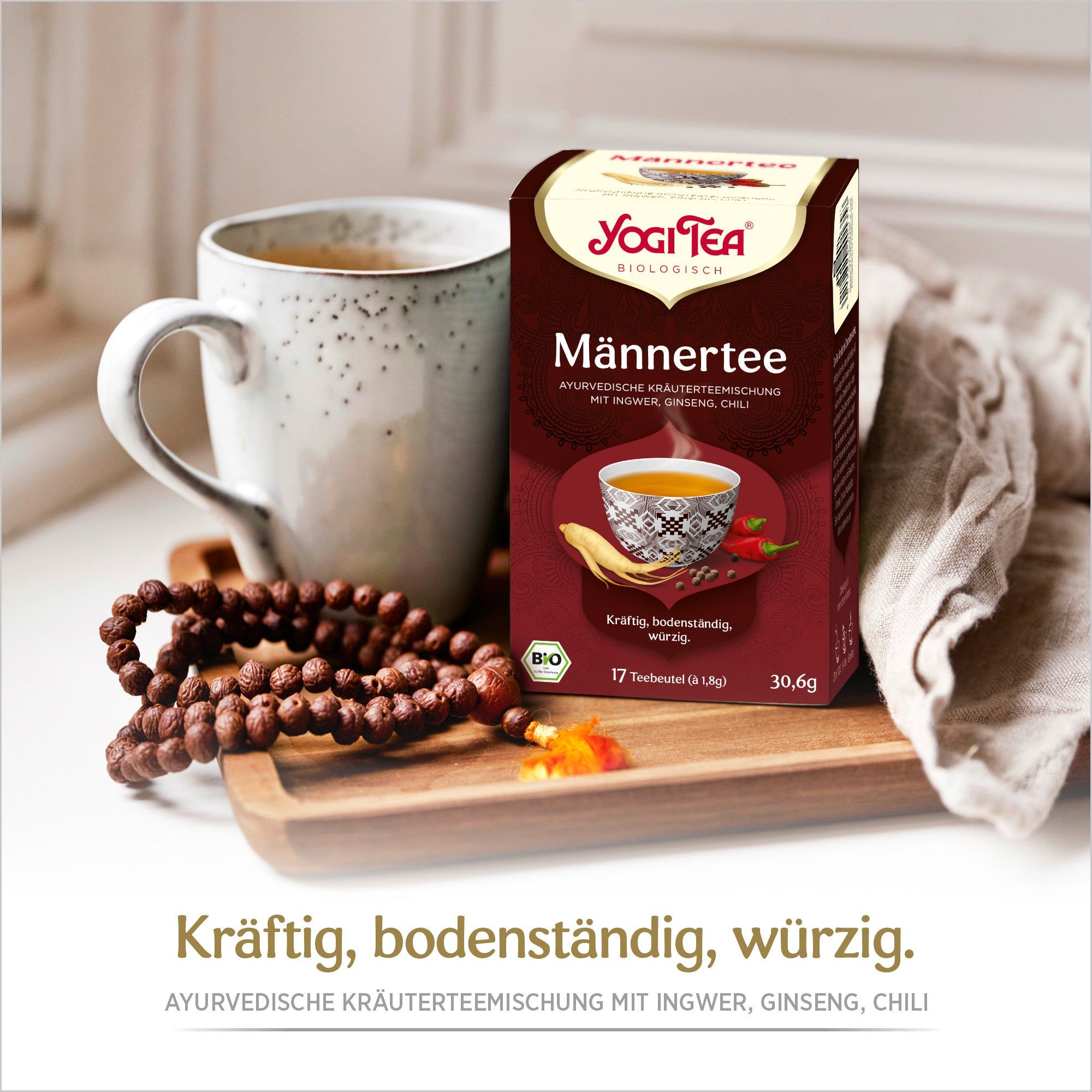 Yogi Tea - Männer Tee Bio Kräutertee Packung neben Tasse Tee und Gebetskette. Aufdrucke: Yogi Tea, Männertee, 17 Teebeutel, Bio-Siegel.