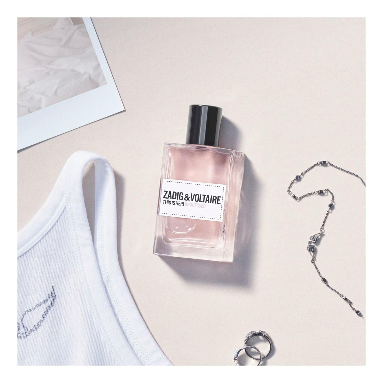 Zadig & Voltaire This is Her! Undressed EdP Nat. Spray. Flakon neben Tanktop, Schmuck und Ringen. Weißes Etikett mit Produktnamen.