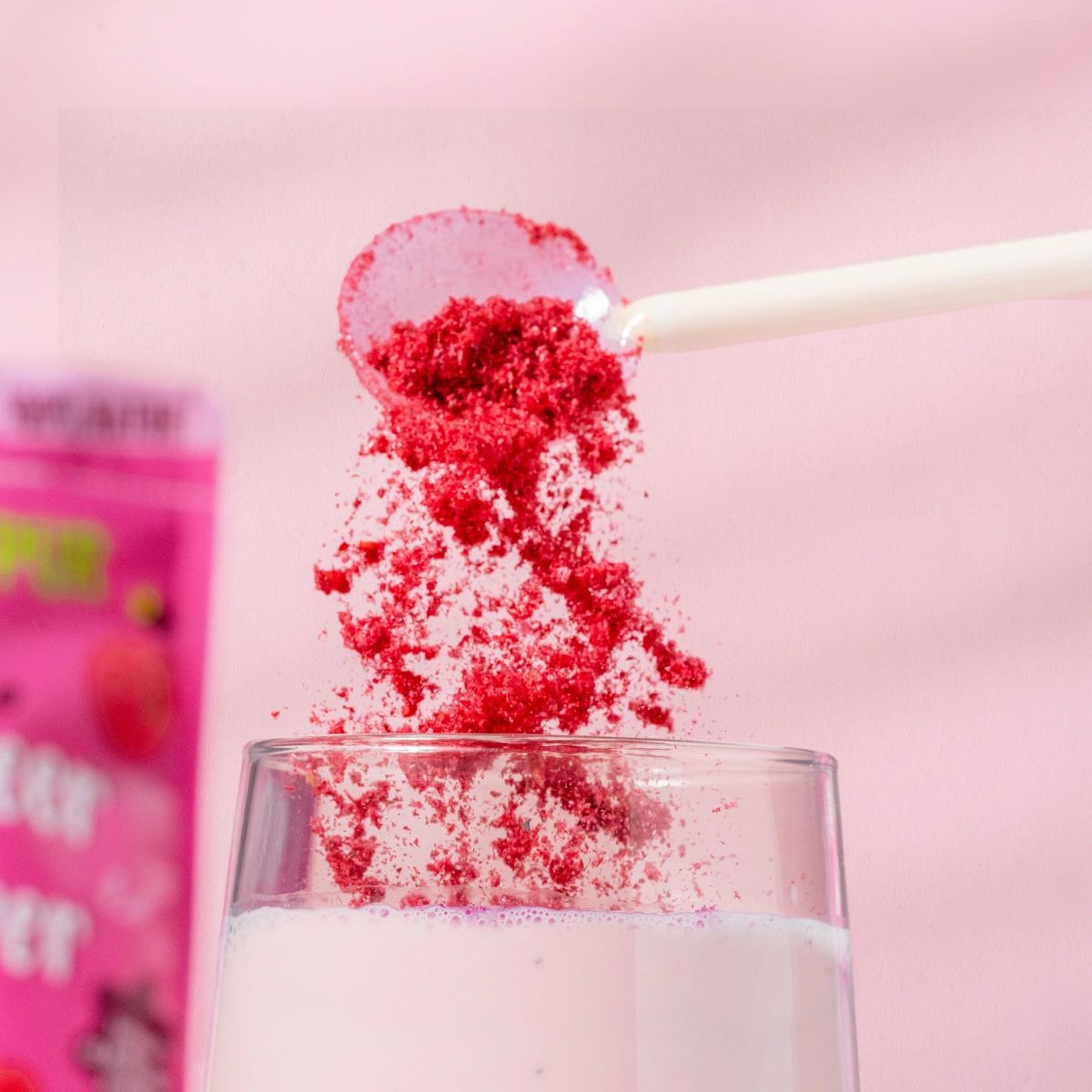 Himbeerpulver wird mit einem Löffel in ein Glas mit rosa Flüssigkeit gegeben.