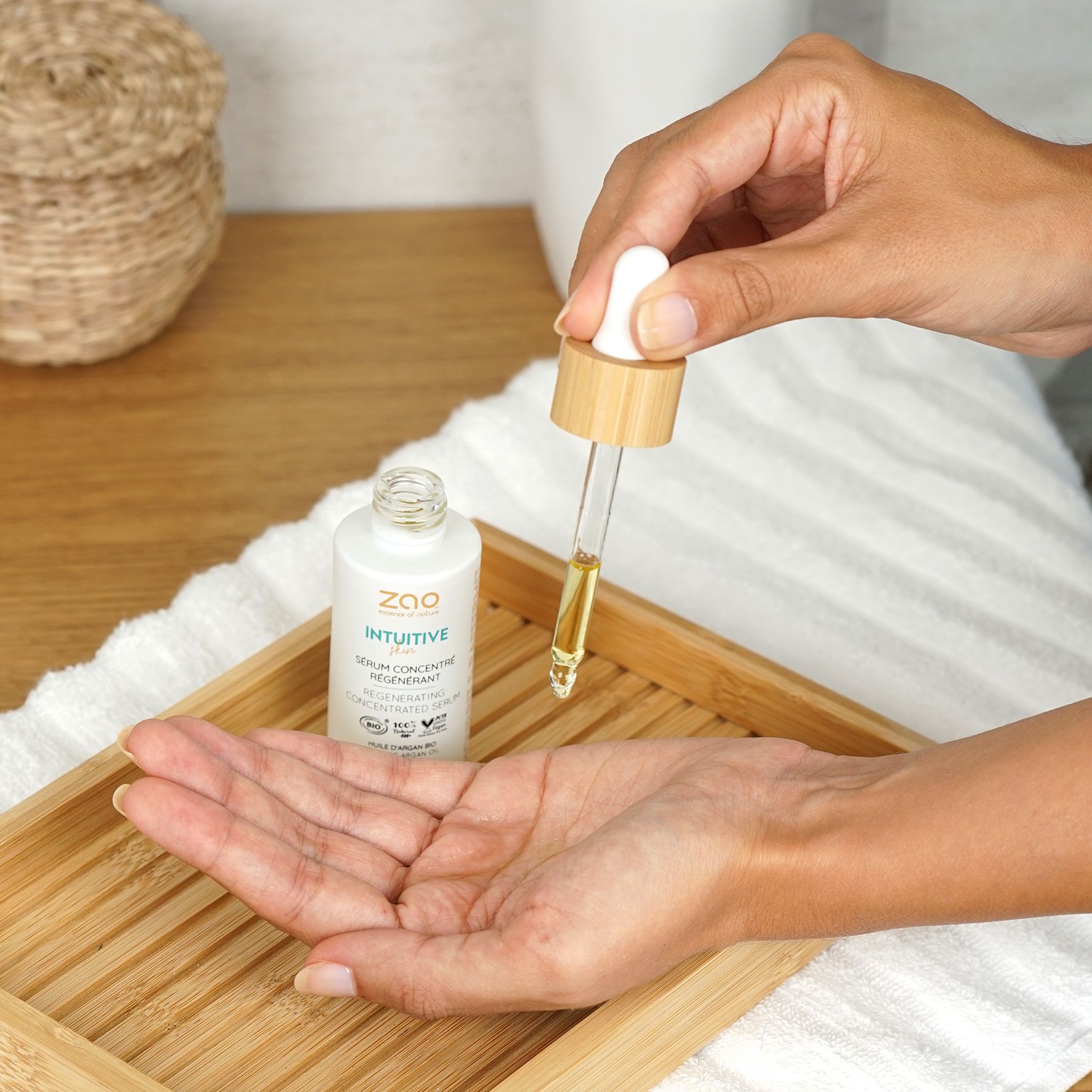 Weißes Fläschchen mit Pipette. Tropfen Serum auf Hand. Aufschrift: ZAO, Intuitive, Serum concentré régénérant. Auf Holztablett.