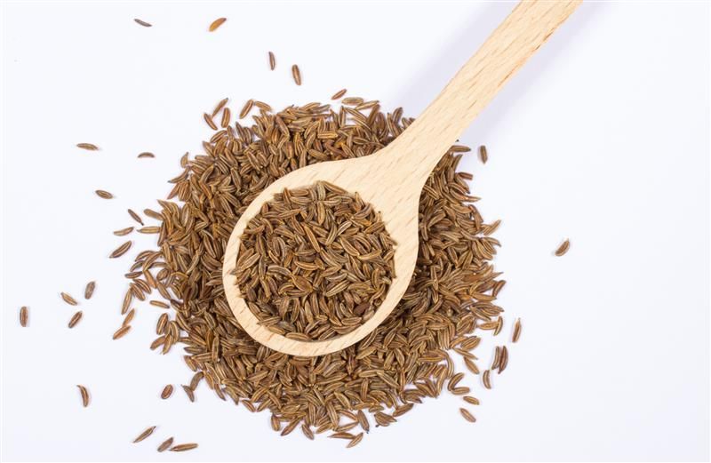 Haufen Kreuzkümmel-Samen mit Holzlöffel. Löffel gefüllt mit Samen, umgeben von Samen auf weißem Hintergrund.