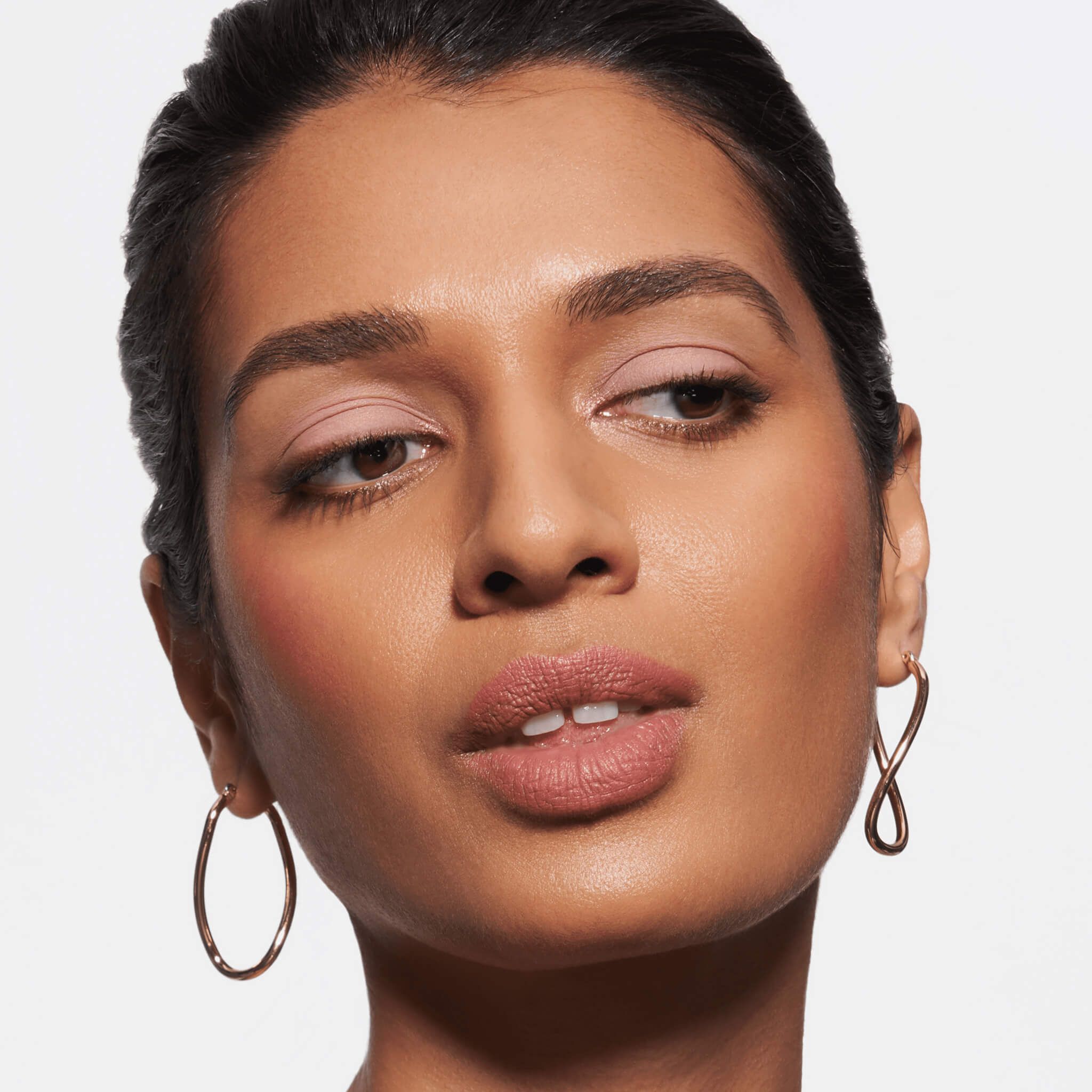 Porträt einer Frau mit rosafarbenem Make-up und goldenen Ohrringen.