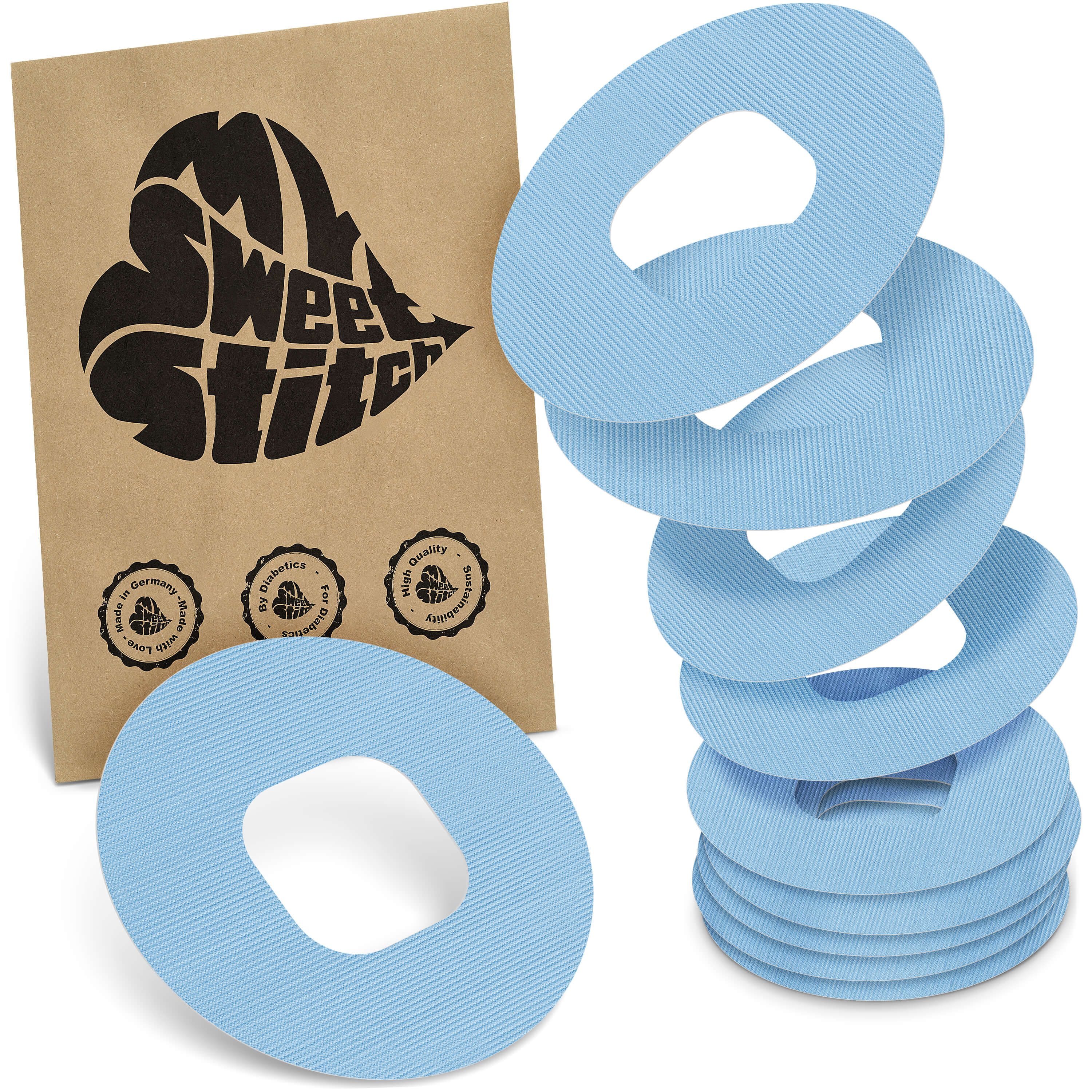 Hellblaue, ringförmige Pflaster mit zentraler Öffnung. Neben einer braunen Verpackung mit Logo und Qualitätssiegeln gestapelt.