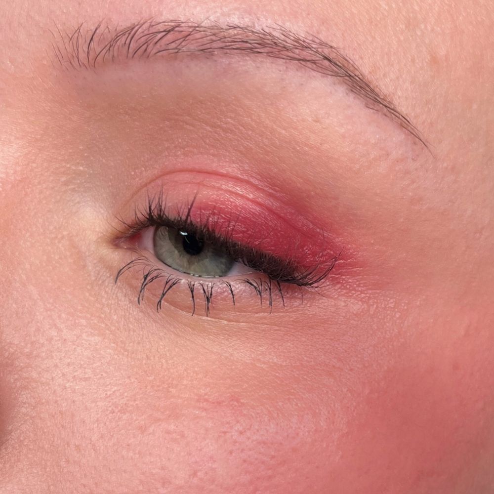 Nahaufnahme eines Auges mit rotem Lidschatten und Wimperntusche. Hautfarbener Hintergrund.