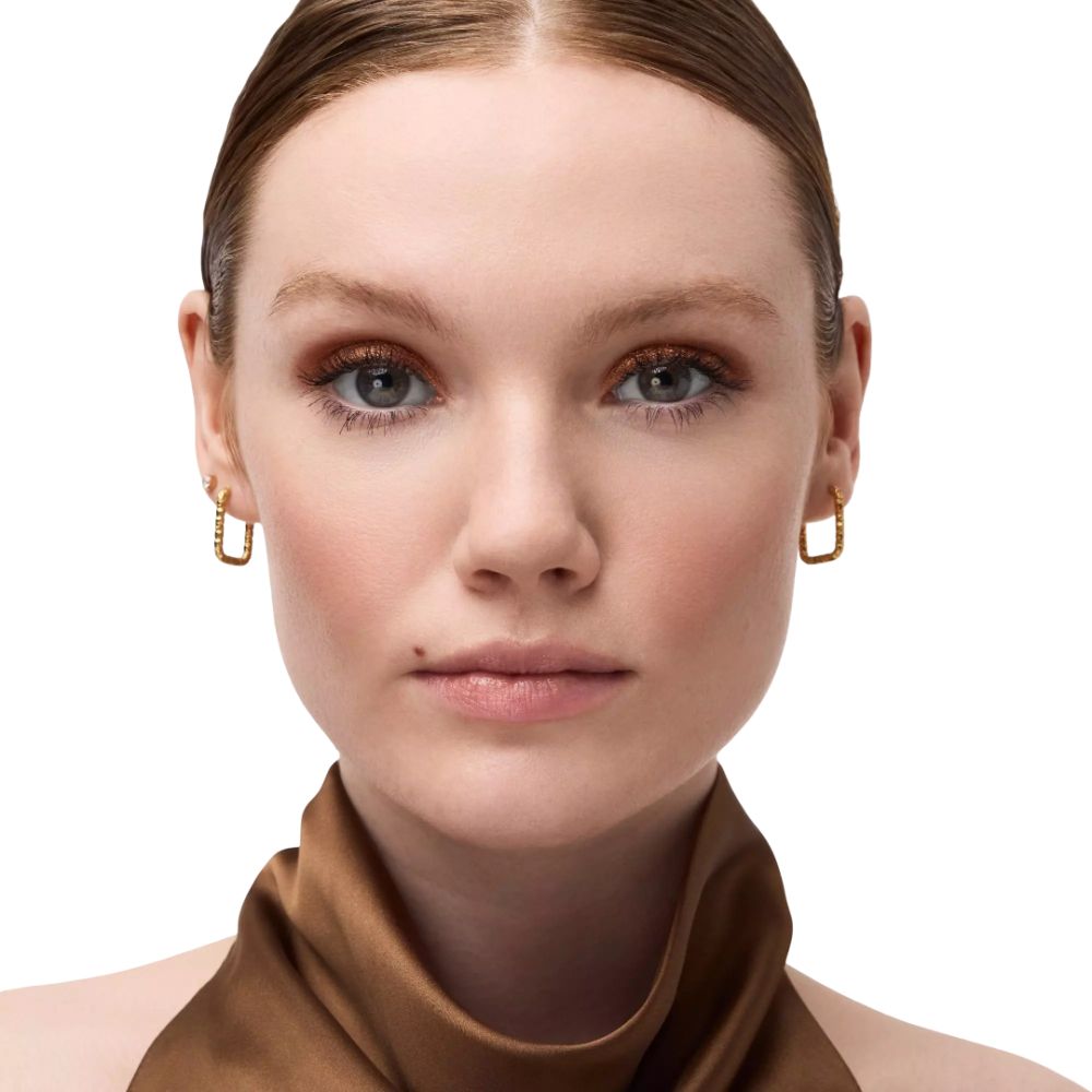 Nahaufnahme eines Gesichts mit goldfarbenem Lidschatten. Hautton hell, goldene Ohrringe.