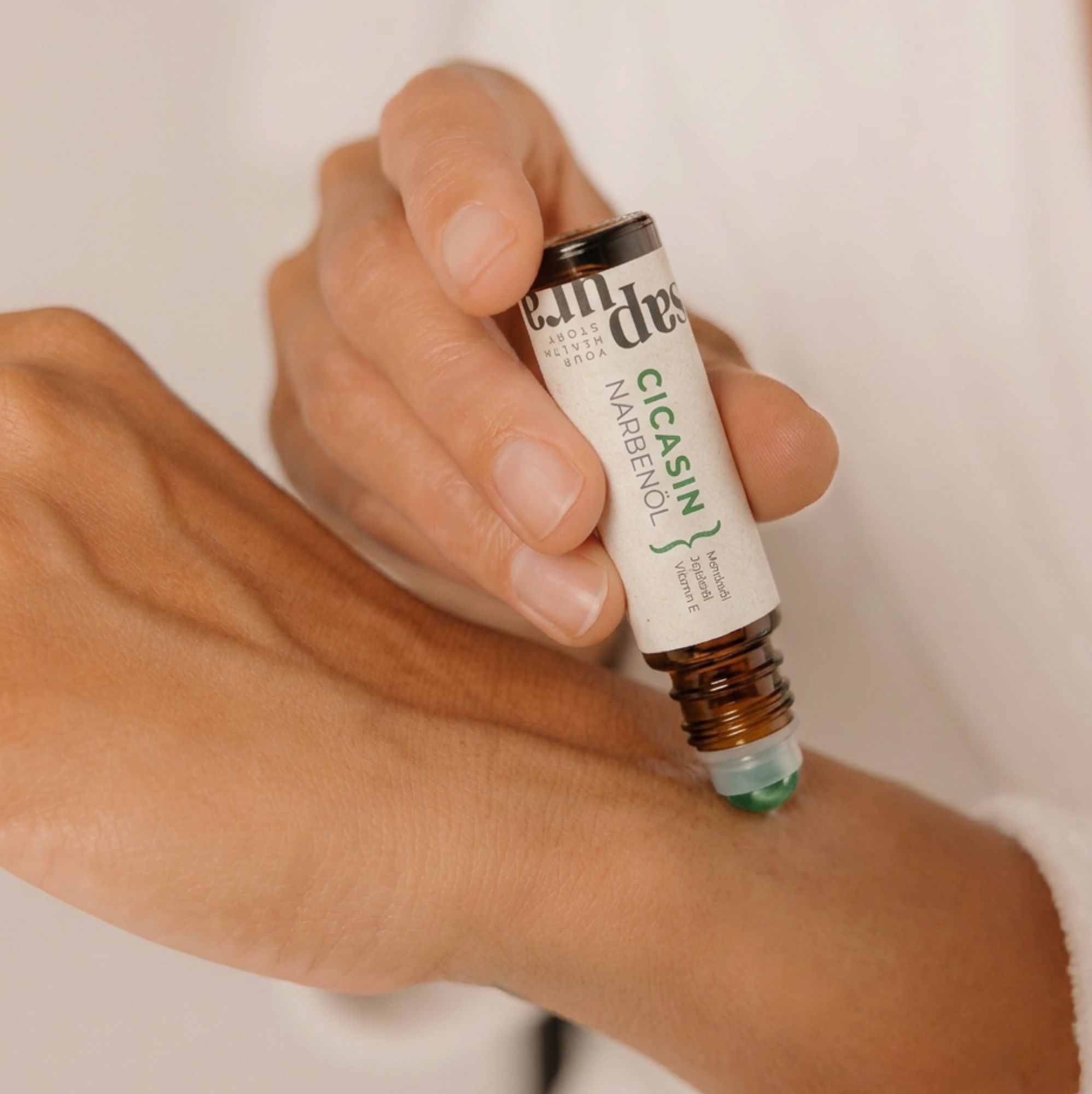 Hand rollt Narbenöl mit einem Roll-On-Applikator auf die Haut am Handgelenk.