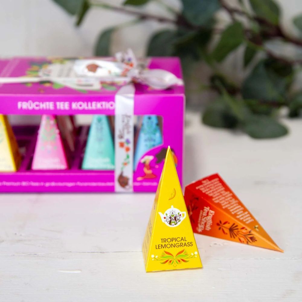 Rosa Tee-Geschenkbox mit Pyramiden-Teebeuteln. Zwei Pyramiden-Teebeutel liegen daneben. Aufschrift: Tropical Lemongrass.