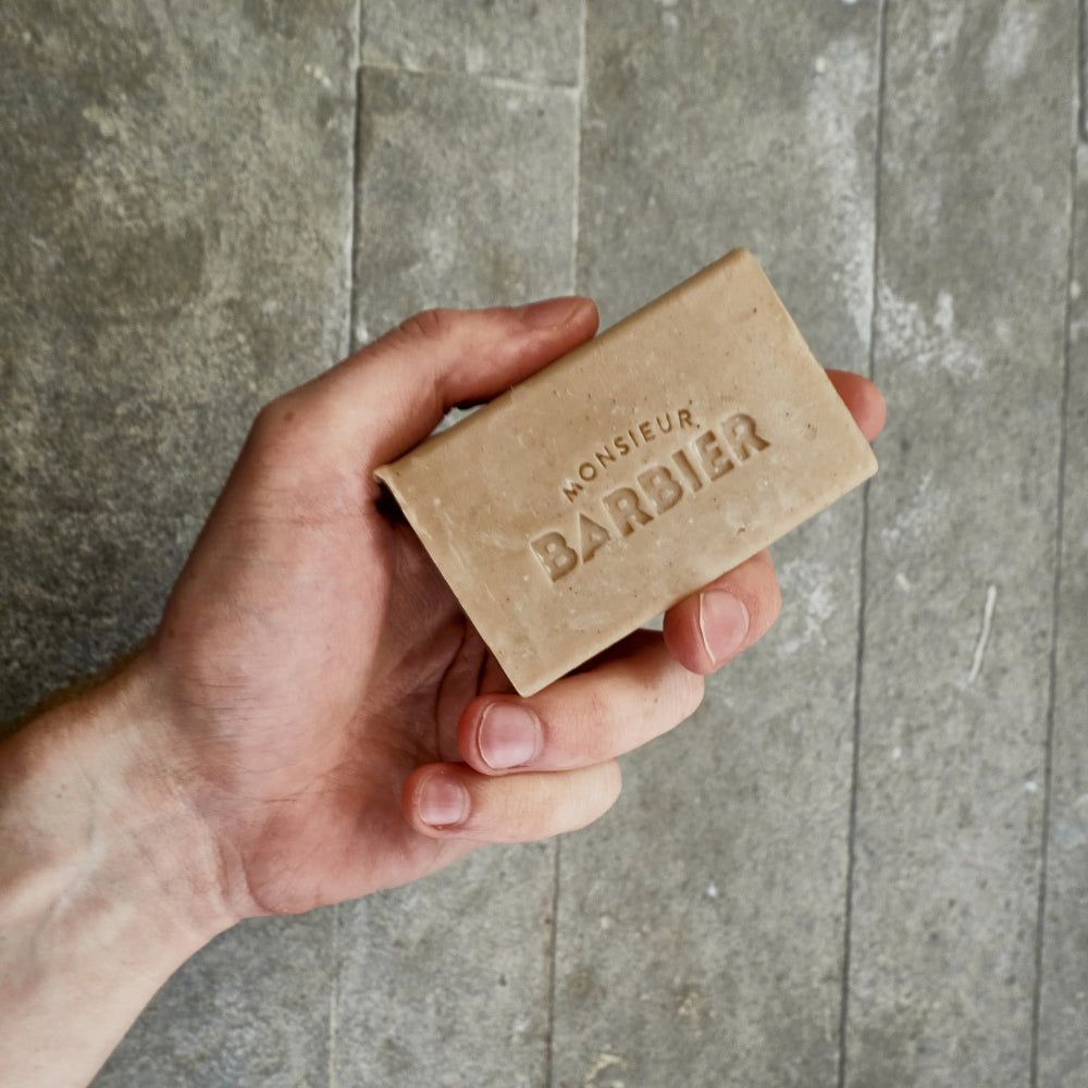 Beige Seife in einer Hand. Auf der Seife steht "MONSIEUR BARBIER".