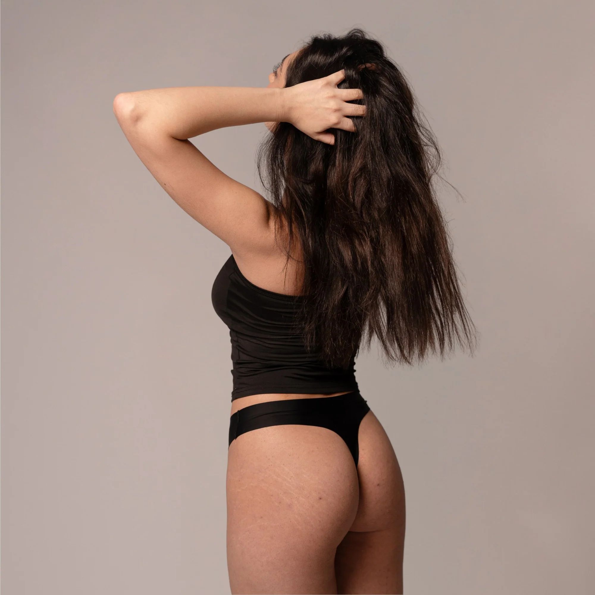 Frau von hinten, schwarzes Top und Slip. Hände im Haar. Hautton sichtbar.