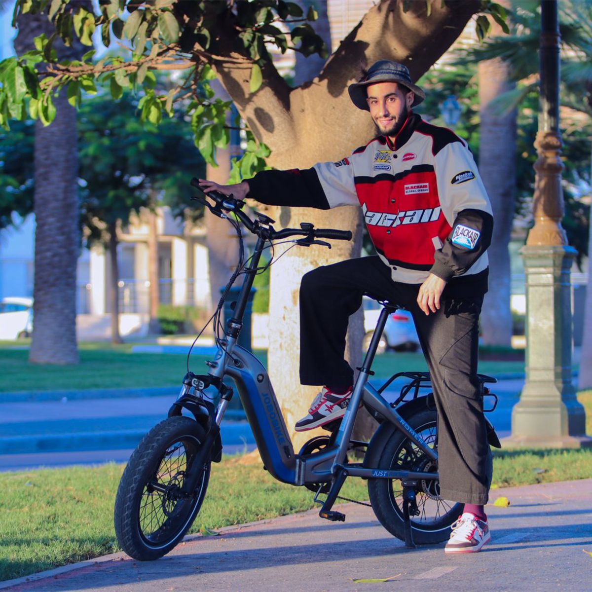 Mann sitzt auf einem blauen JOBOBIKE Romer X E-Bike. Er trägt eine Jacke und eine Mütze. Das Fahrrad steht auf einem Weg.