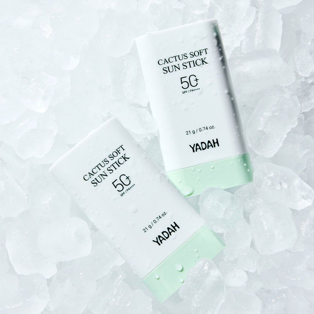 Zwei weiße Sonnenschutzstifte mit grünen Enden liegen auf Eiswürfeln. Auf den Stiften steht 'CACTUS SOFT SUN STICK 50'.