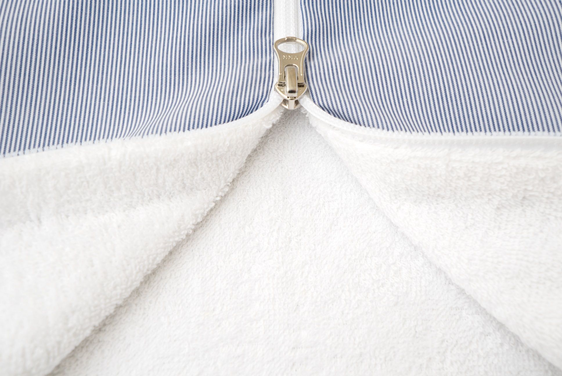 Nahaufnahme des Reißverschlusses eines Schlafsacks. Außenstoff blau-weiß gestreift, Innenfutter weiß.