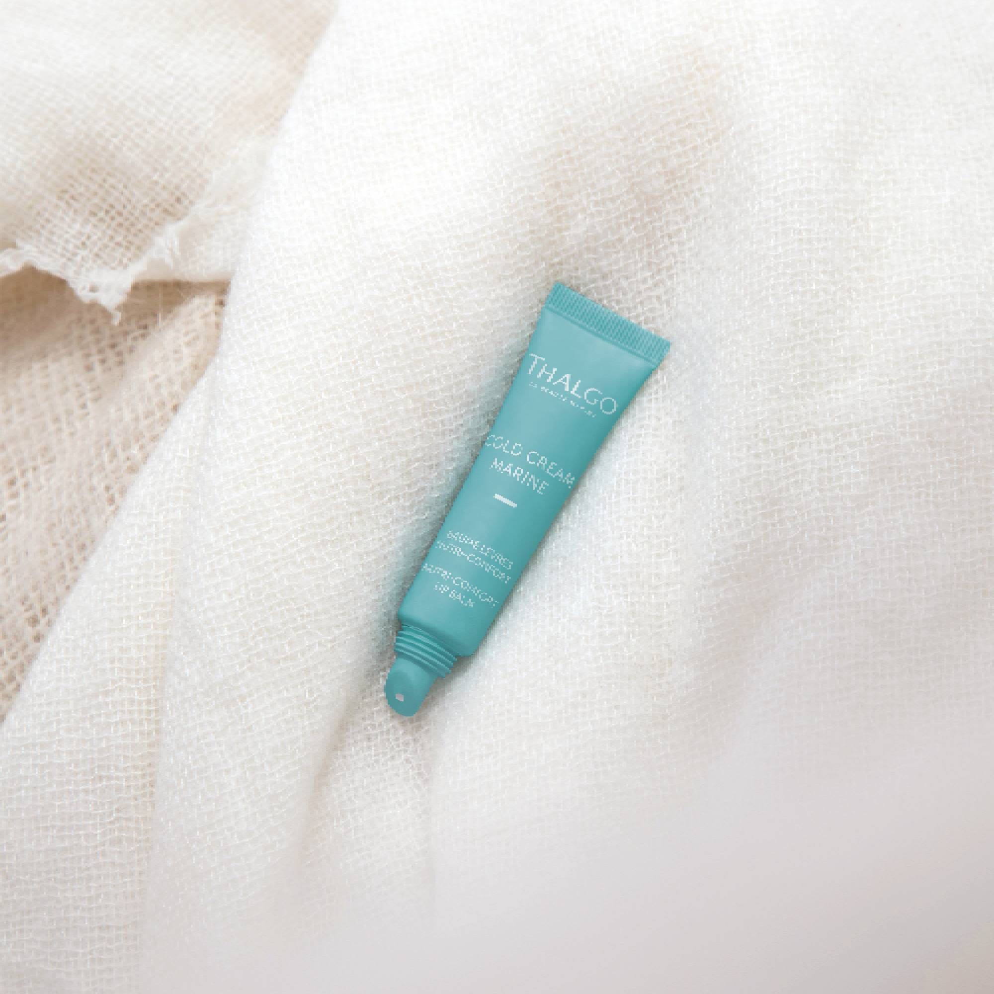 Türkisfarbene Tube auf weißem Stoff. Enthält "THALGO", "COLD CREAM MARINE", "BAUME LEVRES NUTRI-CONFORT".