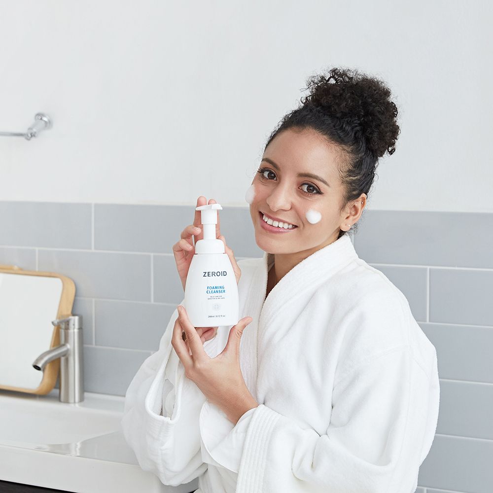 Frau hält eine weiße ZEROID-Schaumreiniger-Flasche. Aufschrift: FOAMING CLEANSER, 240ml/8.12 fl oz.