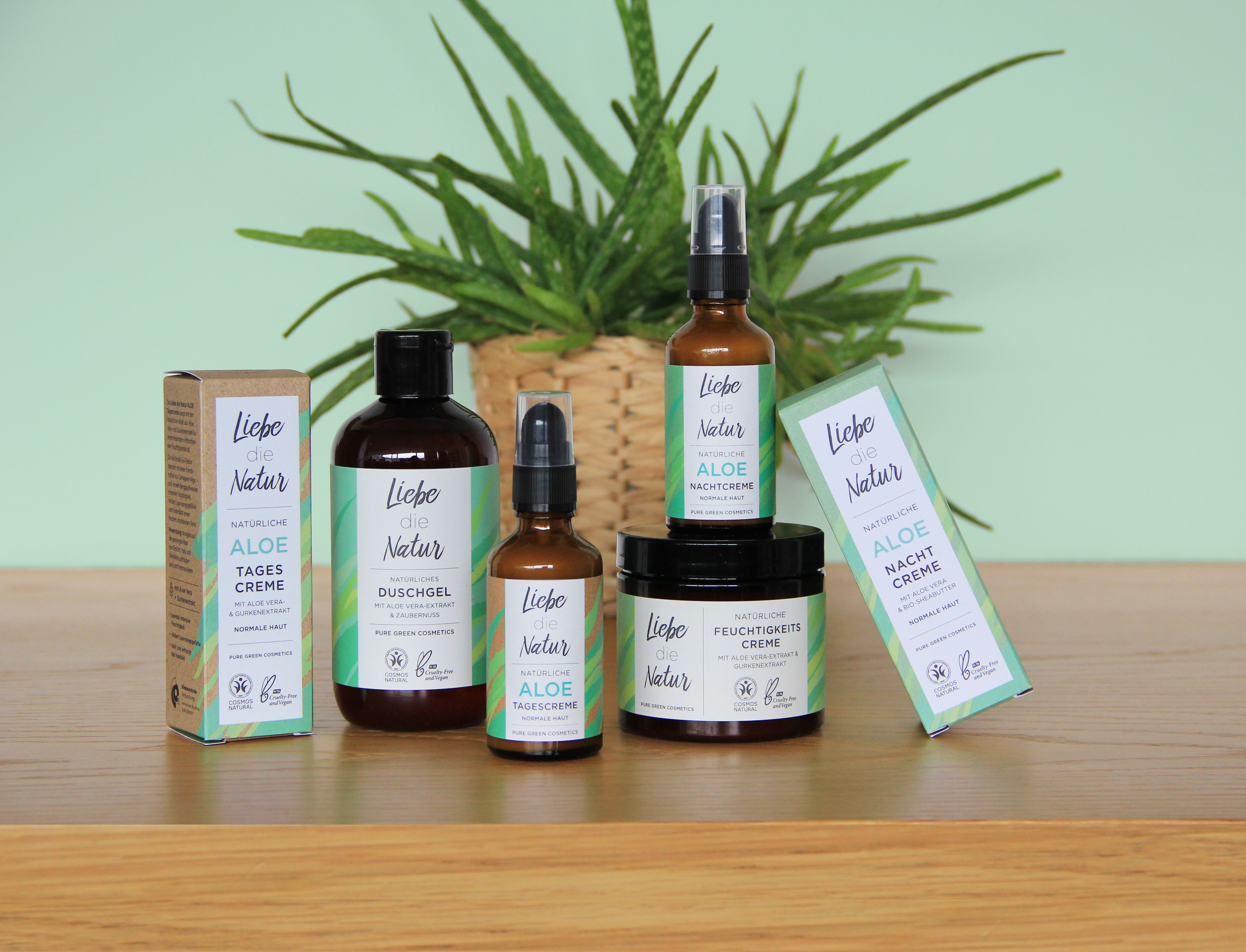 Verschiedene Kosmetikprodukte, darunter Duschgel, in braunen Glasflaschen und Tiegeln. Grün-weiße Etiketten. Pflanzen im Hintergrund.