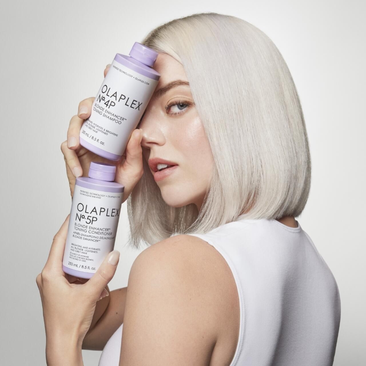 Frau hält zwei Olaplex-Flaschen. Eine No.4P Blonde Enhancer Shampoo und eine No.5P Blonde Enhancer Toning Conditioner. Produktnamen sichtbar.