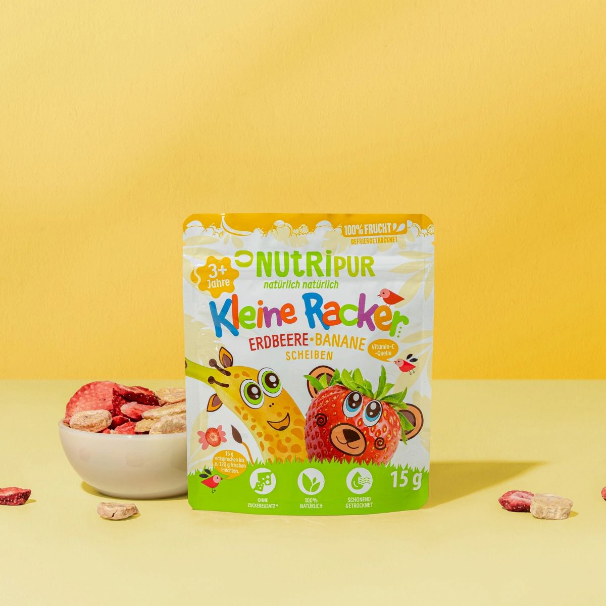 Verpackung mit gefriergetrockneten Früchten und Schale. Aufschrift: NutriPur, Kleine Racker Erdbeere-Banane. Schale mit Früchten.