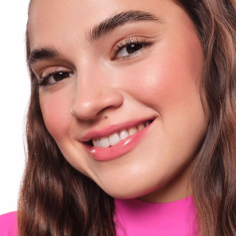 Porträt einer lächelnden Frau mit rosa Lippen und Wangen. Sie trägt ein pinkes Oberteil.