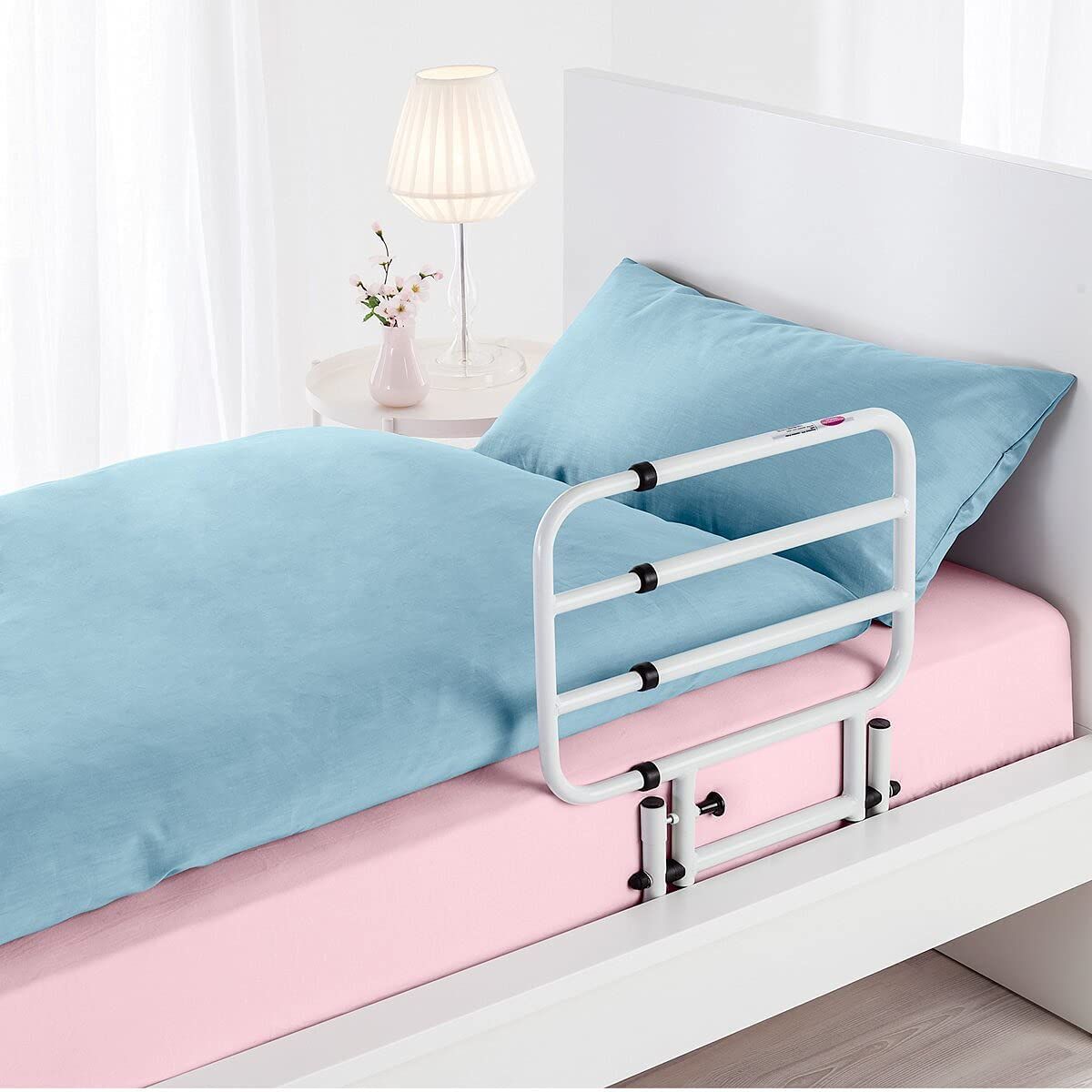 Weißes, ausziehbares Bettgeländer an einem Bett mit blauer Bettwäsche. Schwarze Verbindungsstücke.