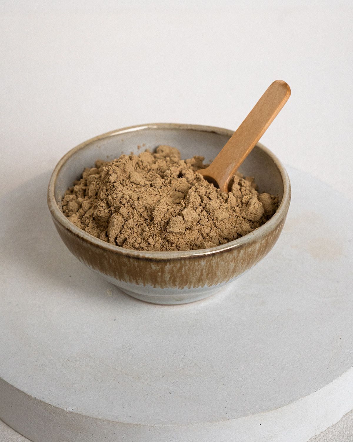 Braune Pulver in einer kleinen, hellbraunen Schale. Ein kleiner Holz-Löffel liegt in der Schale.