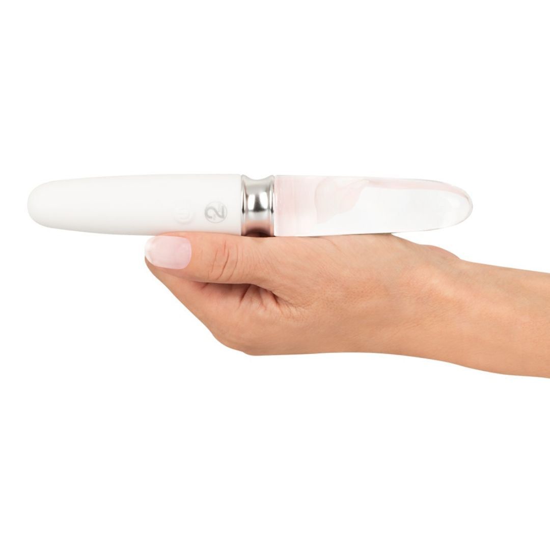 Weißer Vibrator, gehalten in einer Hand. Glas-Ende mit rosa Muster. Silberfarbener Ring.
