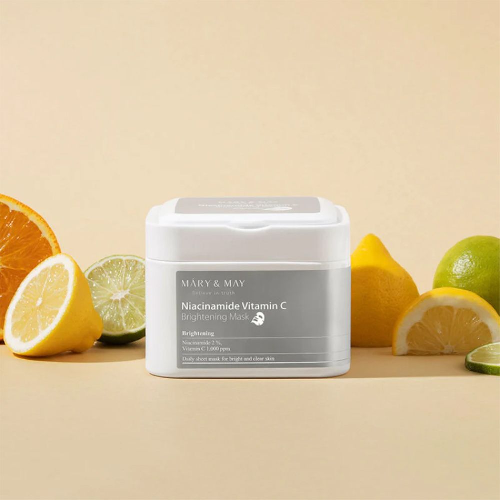 Weißer Behälter mit MARY & MAY Niacinamide Vitamin C Brightening Mask. Zitrusfrüchte umgeben den Behälter.