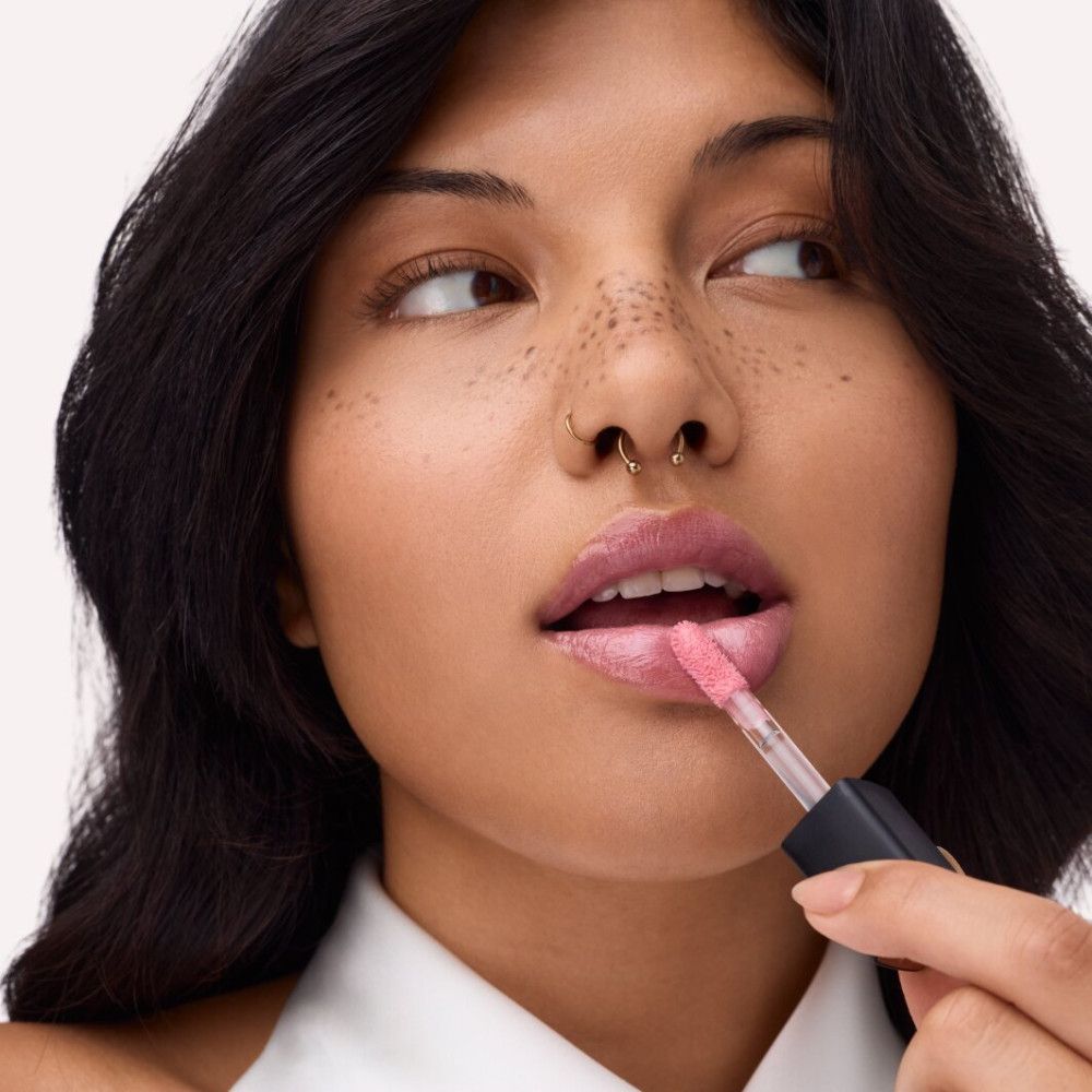 Frau trägt Lipgloss auf. Produkt und Applikator sichtbar. Rosa Farbton.