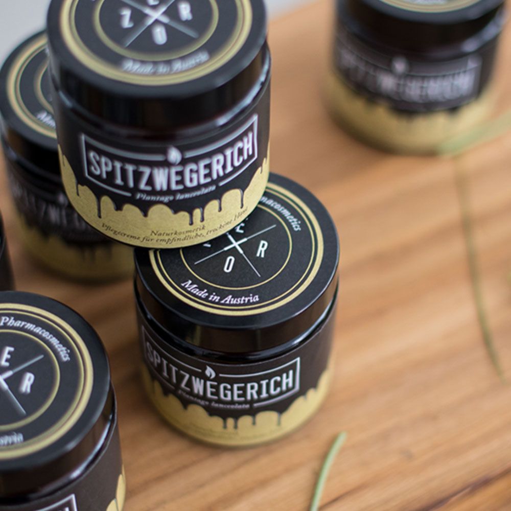 Mehrere Gläser auf Holzbrett. Aufschrift: Spitzwegerich, Plantago lanceolata. Deckel mit Logo und Schriftzug.