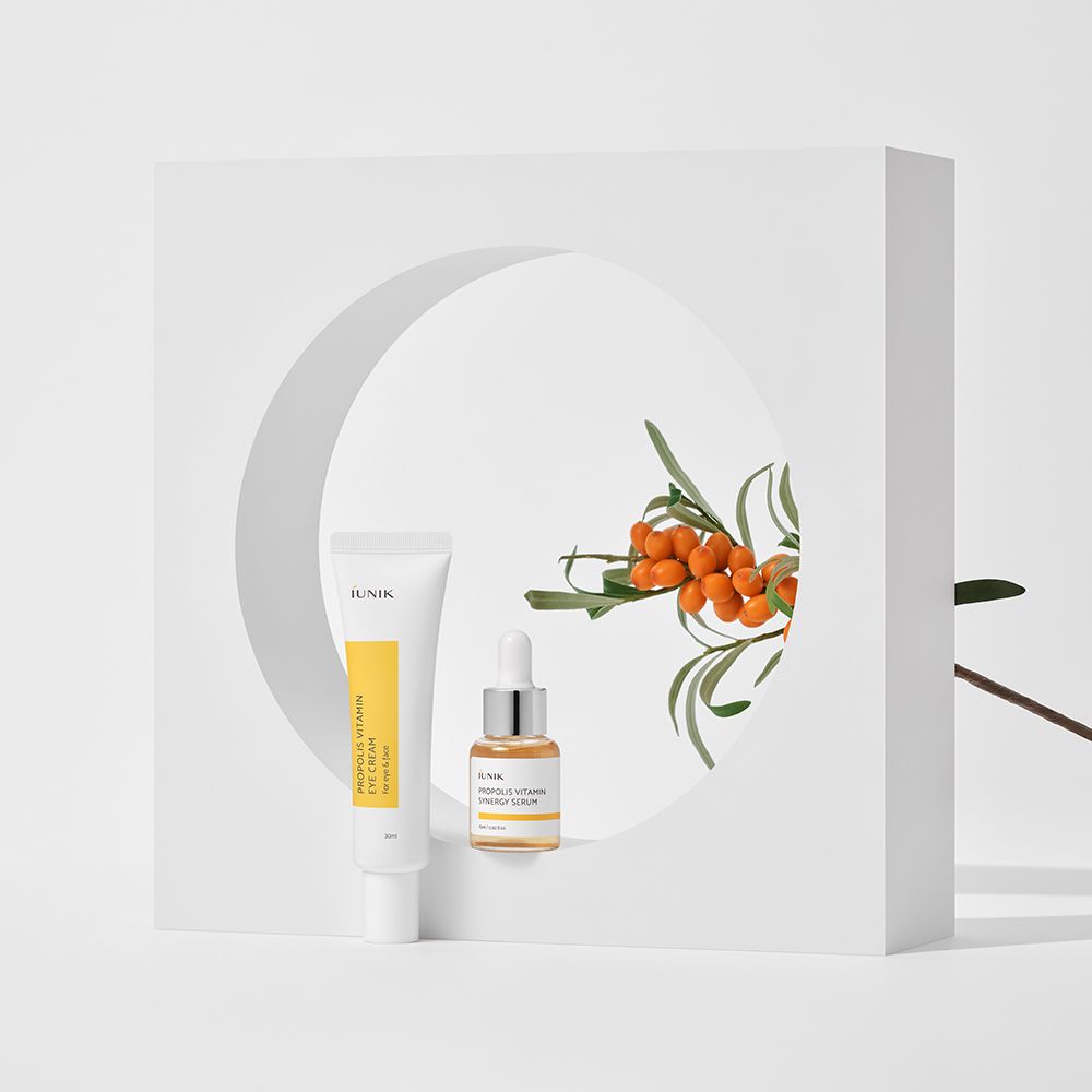 IUNIK Propolis Vitamin Eye Cream Set. Augencreme und Serum neben Zweig mit Beeren. Auf weißem Hintergrund, in weißem Rahmen.