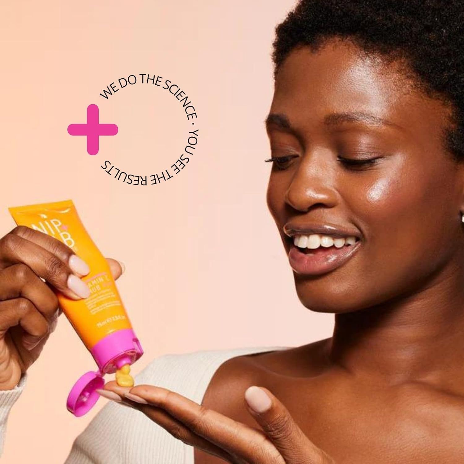 Frau hält eine gelb-orange Tube mit rosa Verschluss. Produkt wird aus der Tube gedrückt.