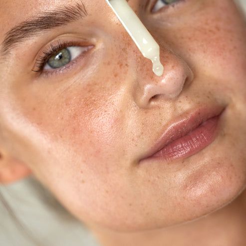 Gesicht einer Frau mit Hautpflege. Eine Pipette tropft Serum auf die Nase. Haut mit Sommersprossen.