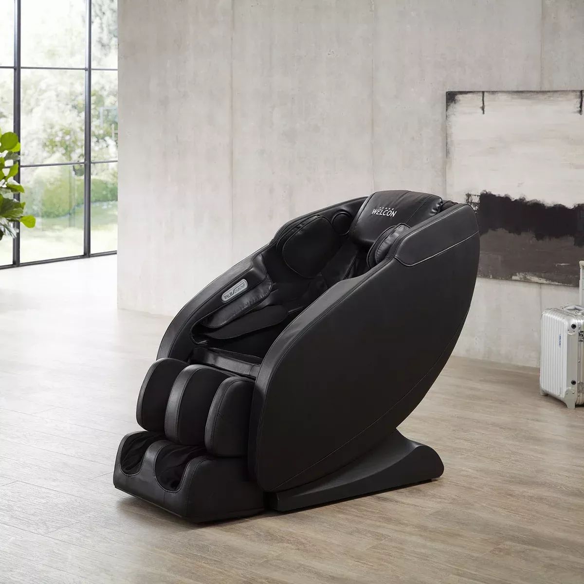 Schwarzer Massagesessel in hellem Raum. Integrierte Armlehnen, Fußstütze und Kopfstütze. WELCON-Logo.
