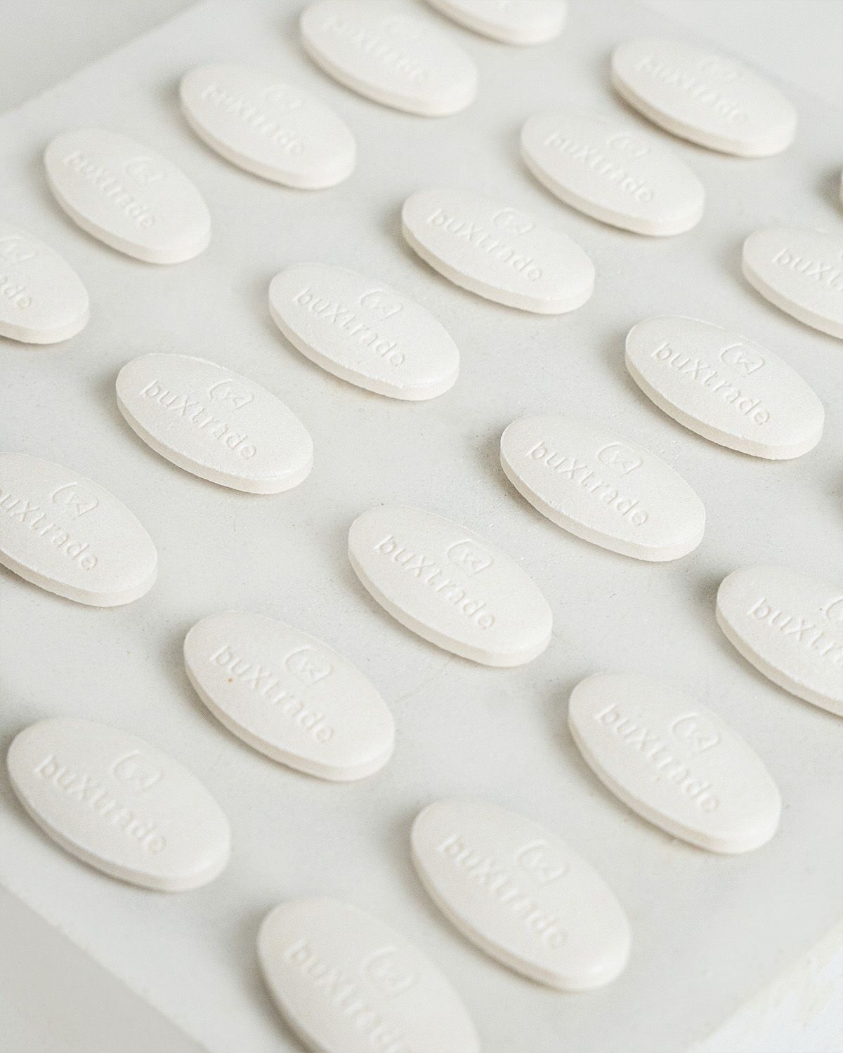 Mehrere weiße, ovale buXtrade Vitamin C Tabletten, nebeneinander auf weißem Untergrund angeordnet.