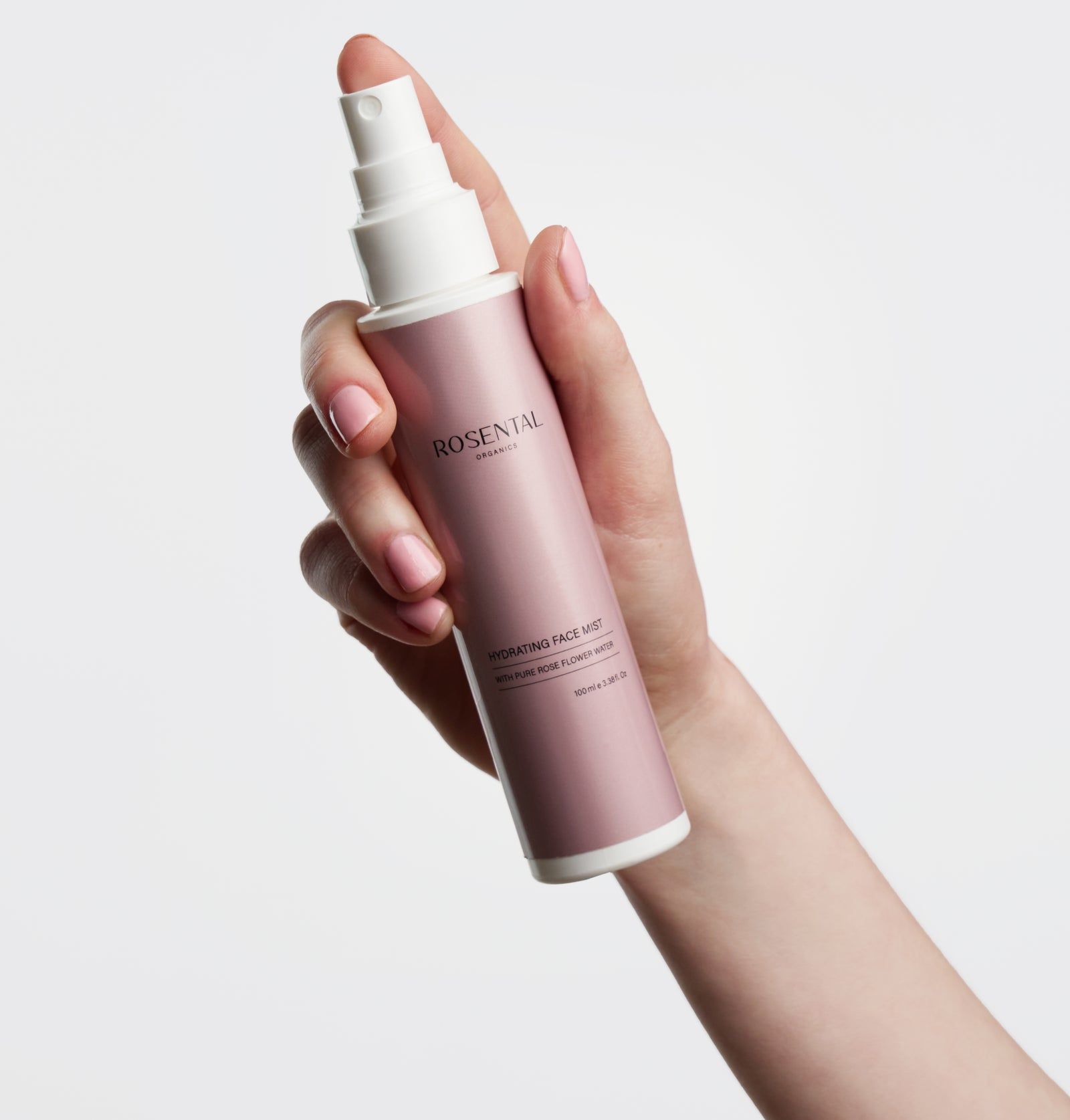 Hand hält Rosental Organics Hydrating Face Mist Flasche. Rosa Etikett mit weißem Sprühkopf. Text: Hydrating Face Mist.