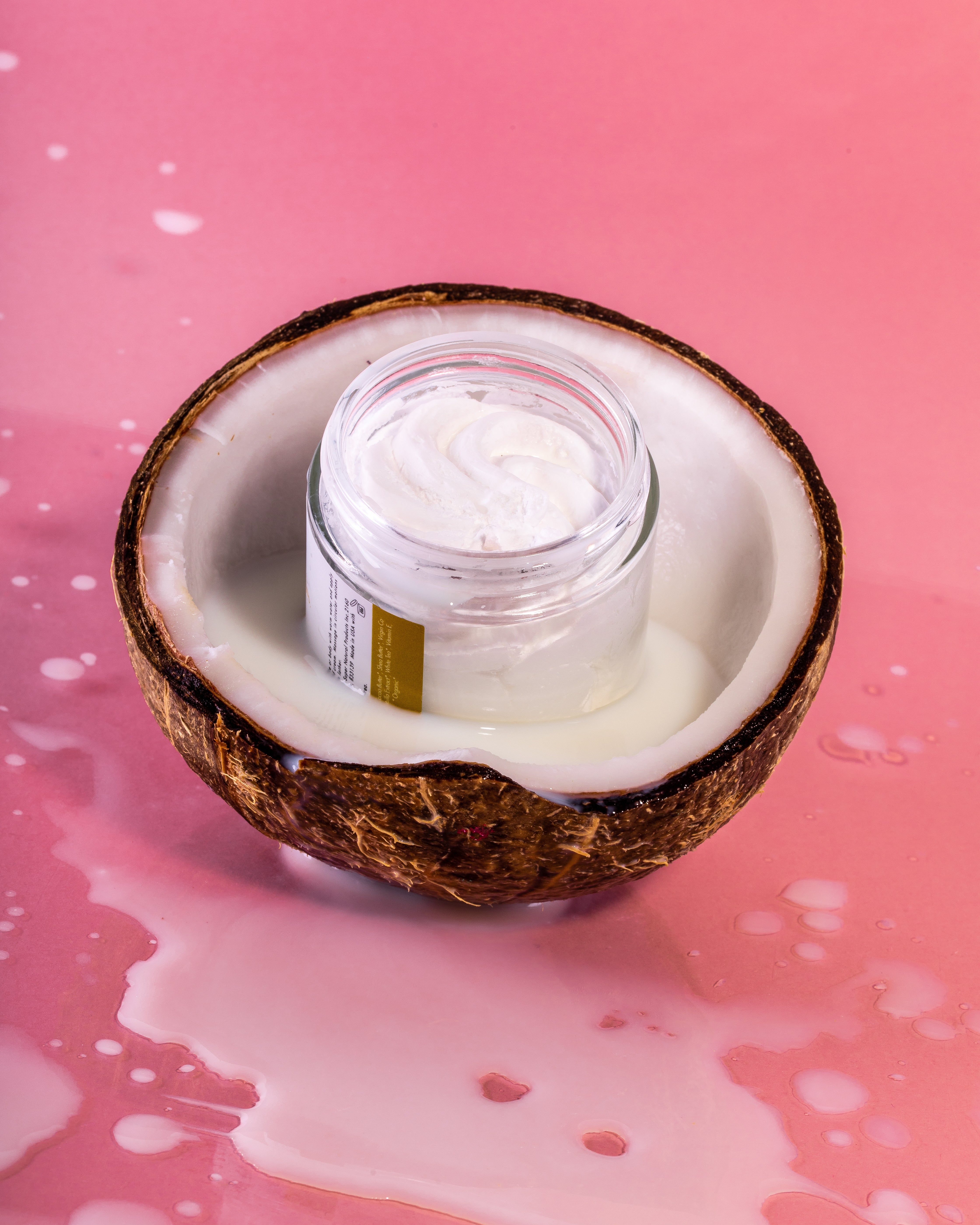 Kleiner Glasbehälter mit Rasierbutter in einer halben Kokosnuss. Rosa Hintergrund.