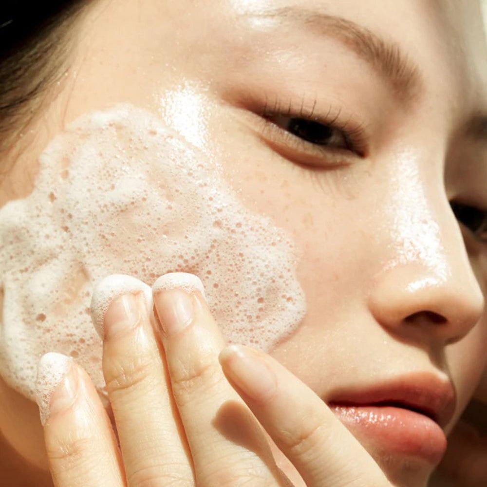 Frau trägt Schaum auf. Aufschrift: Gentle Black Facial Cleanser. Vegan. Hautpflege.