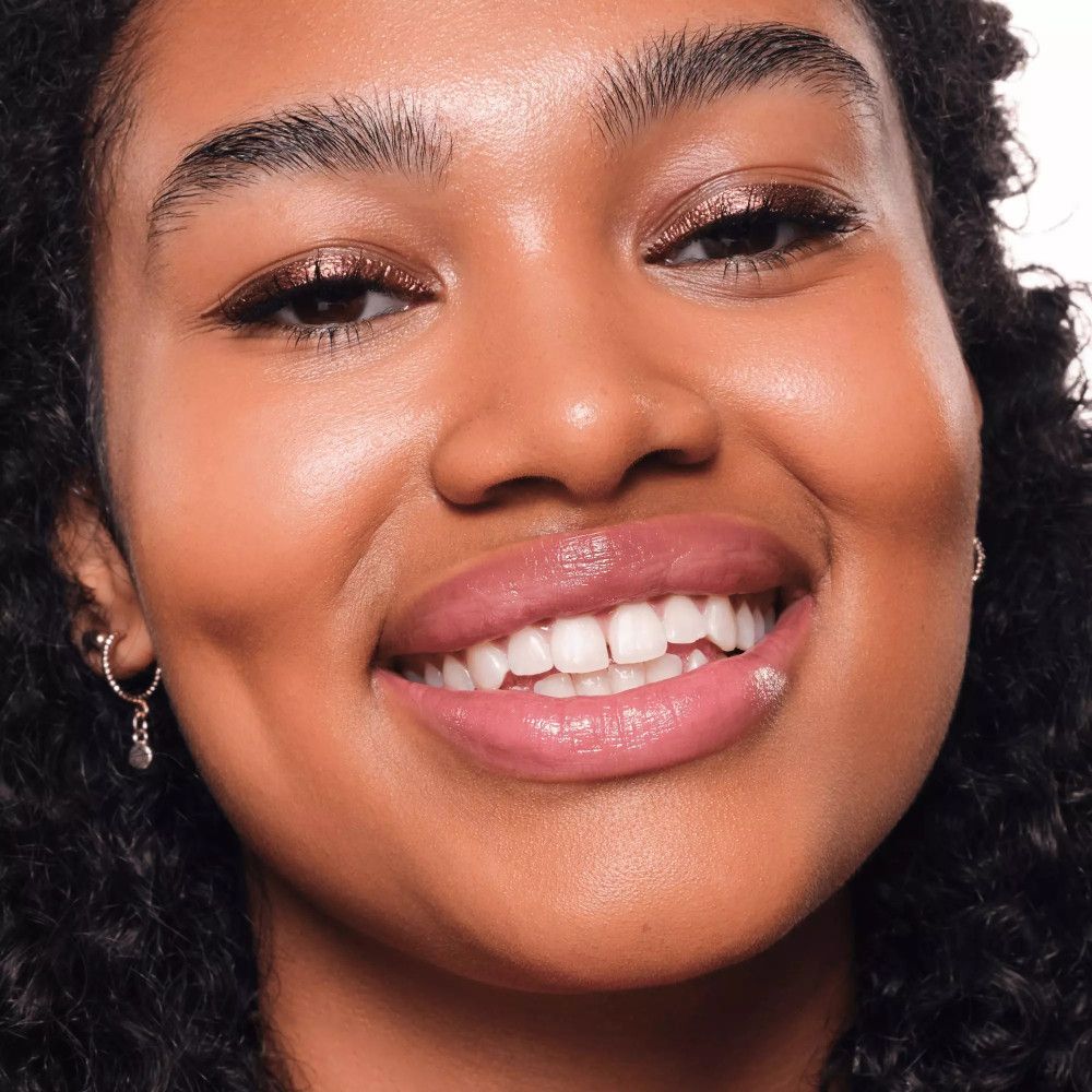 Nahaufnahme einer Frau mit metallischem Eyeliner. Sie lächelt. Sichtbar: Augen, Lippen, Haut.