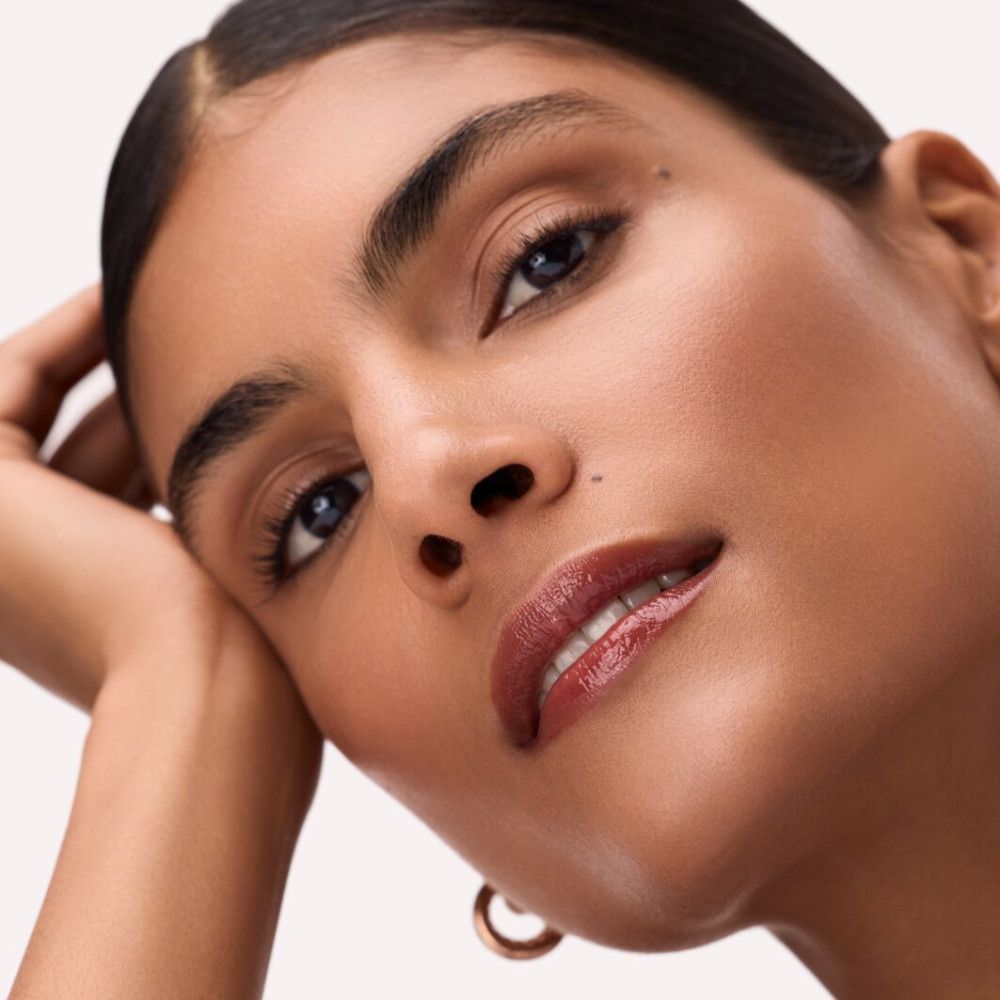 Porträt einer Frau mit Lip Tint auf den Lippen. Sie stützt den Kopf auf die Hand, trägt goldene Creolen.