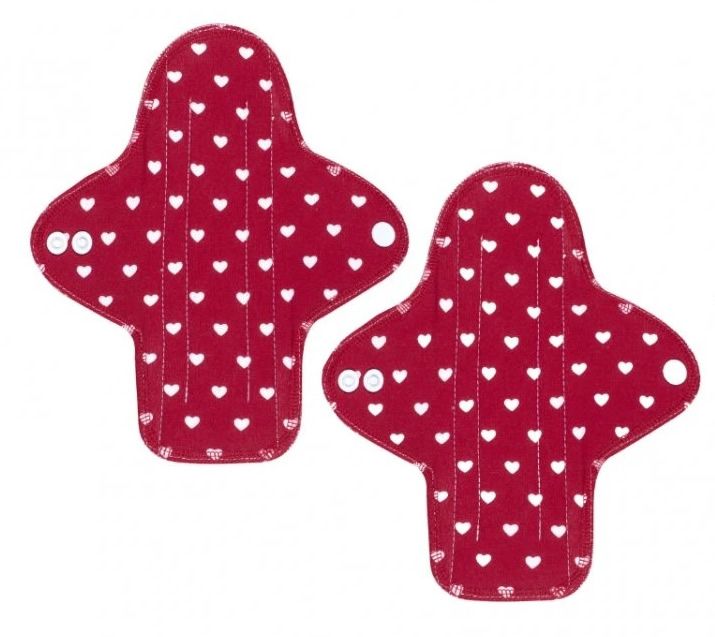 Zwei rote Stoffbinden mit weißen Herzen. Jede Binde hat eine ovale Form mit Flügeln und Druckknöpfen.