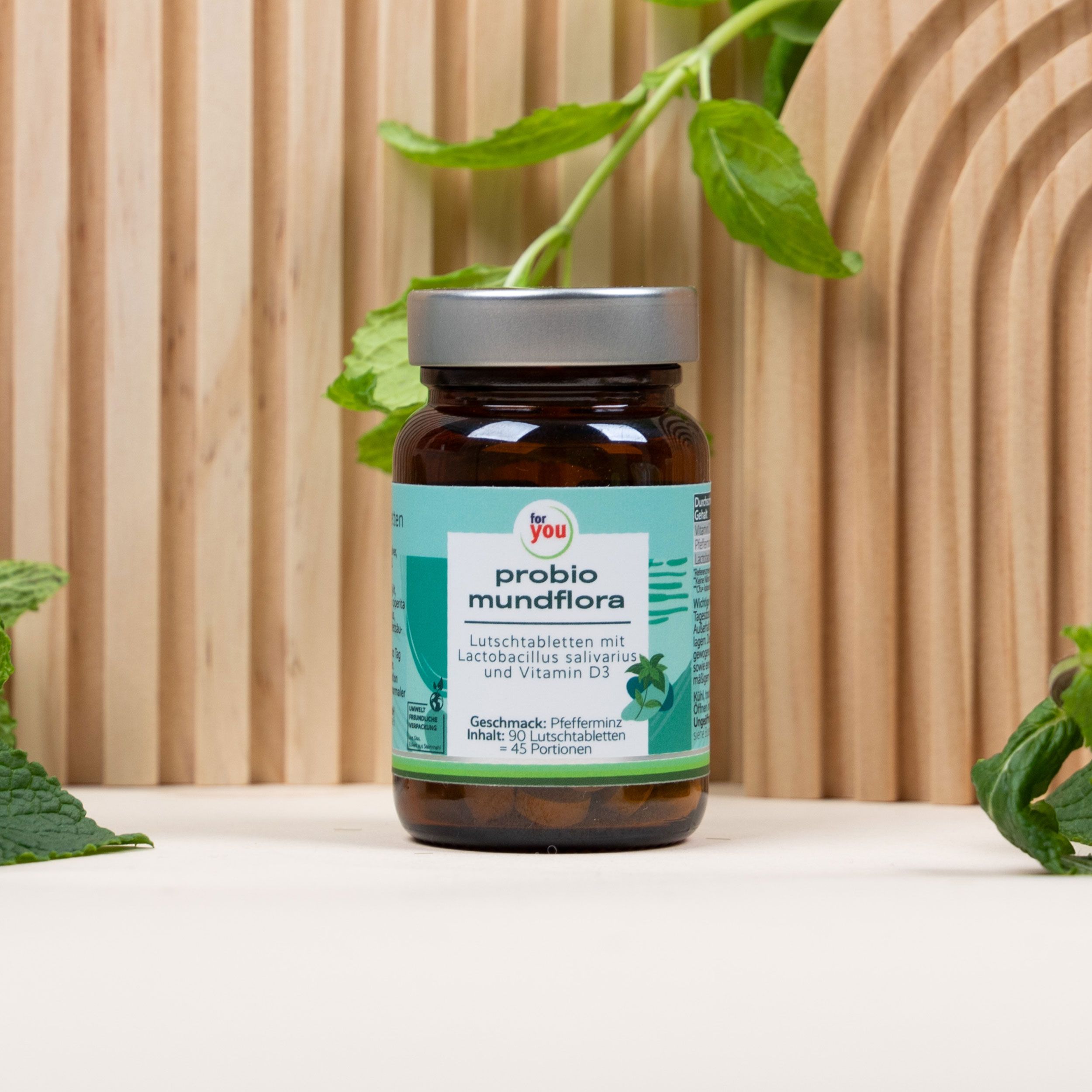 Braune Glasflasche mit Tabletten. Aufschrift: probio mundflora. Türkis-weißes Etikett. Hintergrund: Holz und Blätter.
