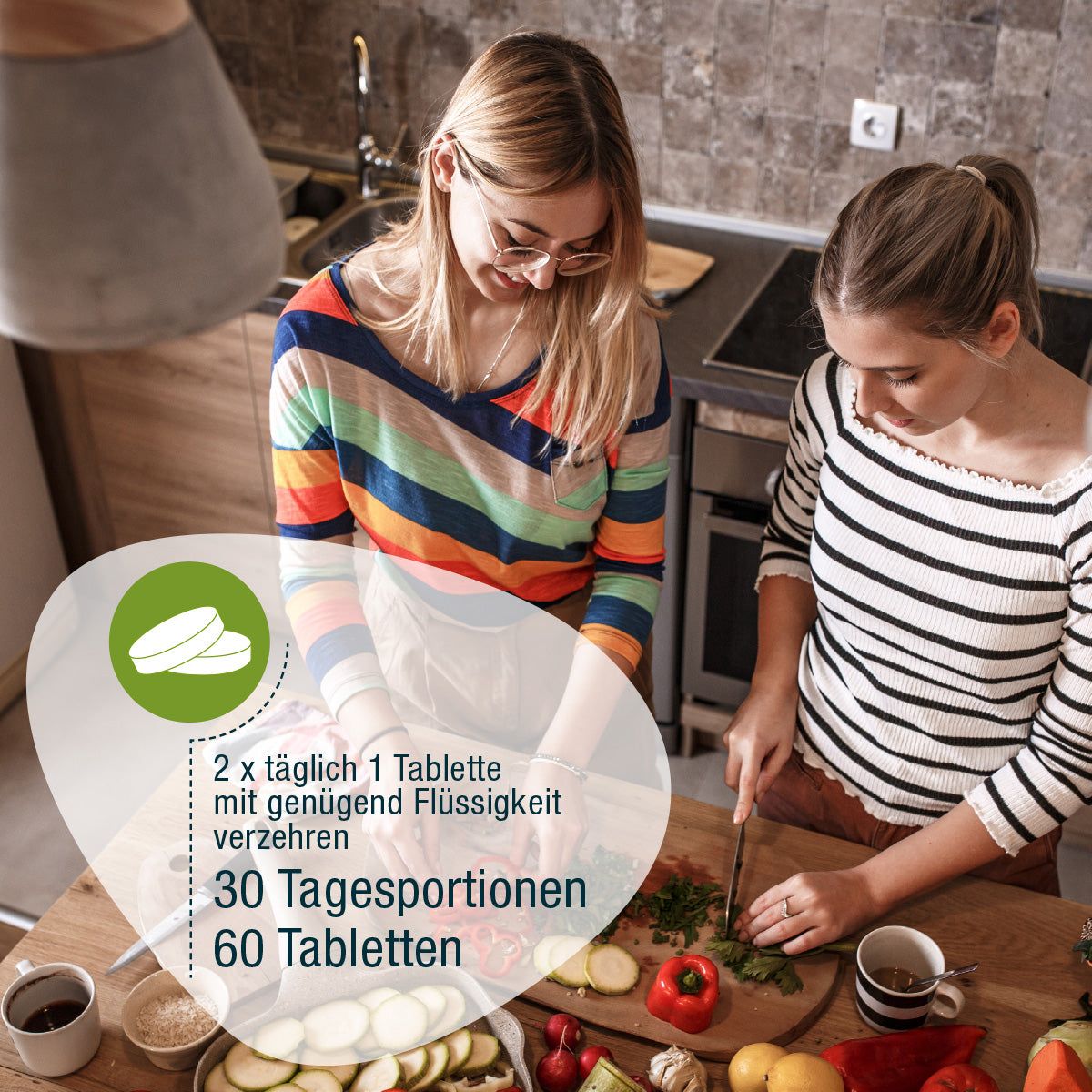 Zwei Frauen in einer Küche. Auf einem Tisch liegen Gemüse und Tabletten. Text: 2 x täglich 1 Tablette mit genügend Flüssigkeit.