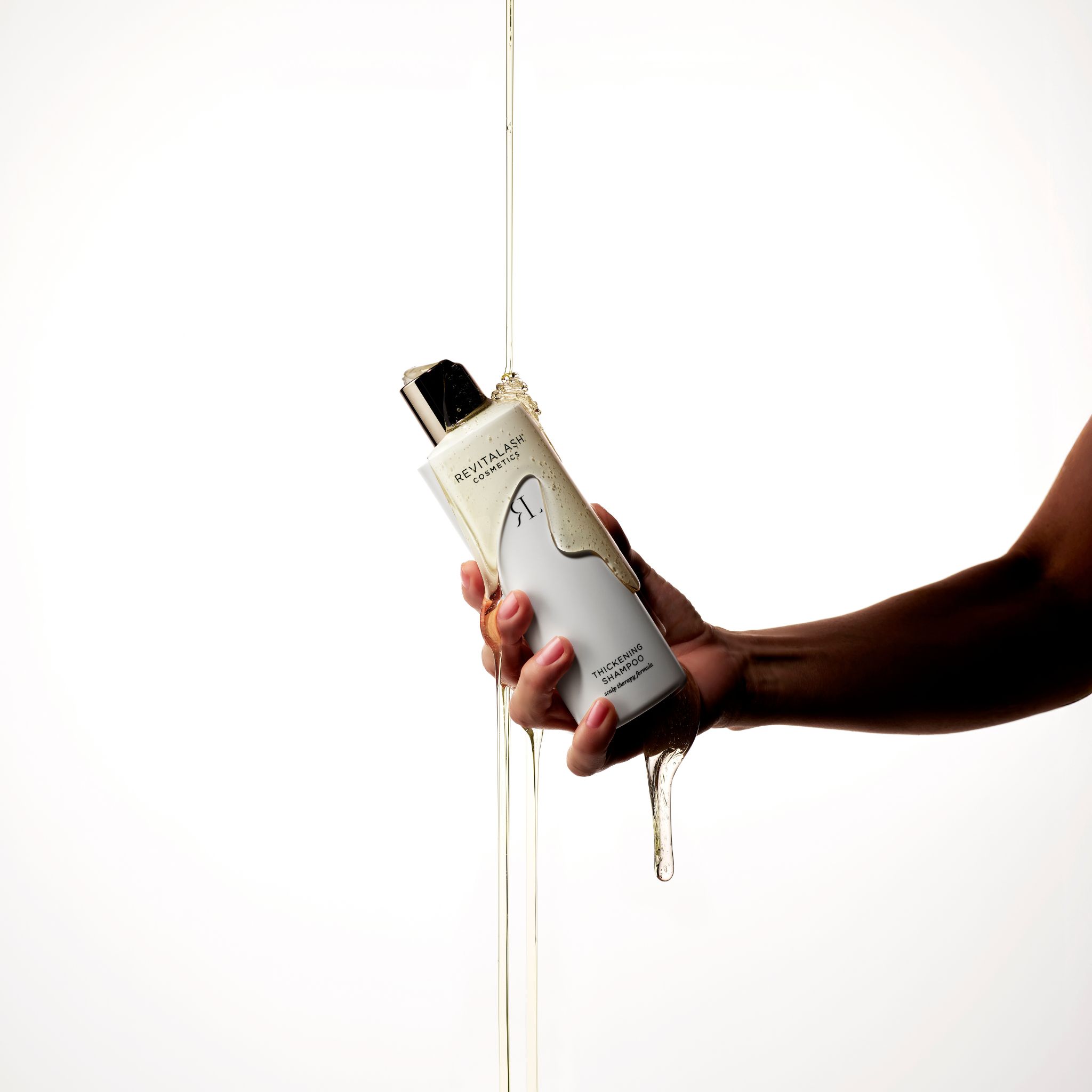 Hand hält RevitaLash Thickening Shampoo, während Shampoo darüber gegossen wird.