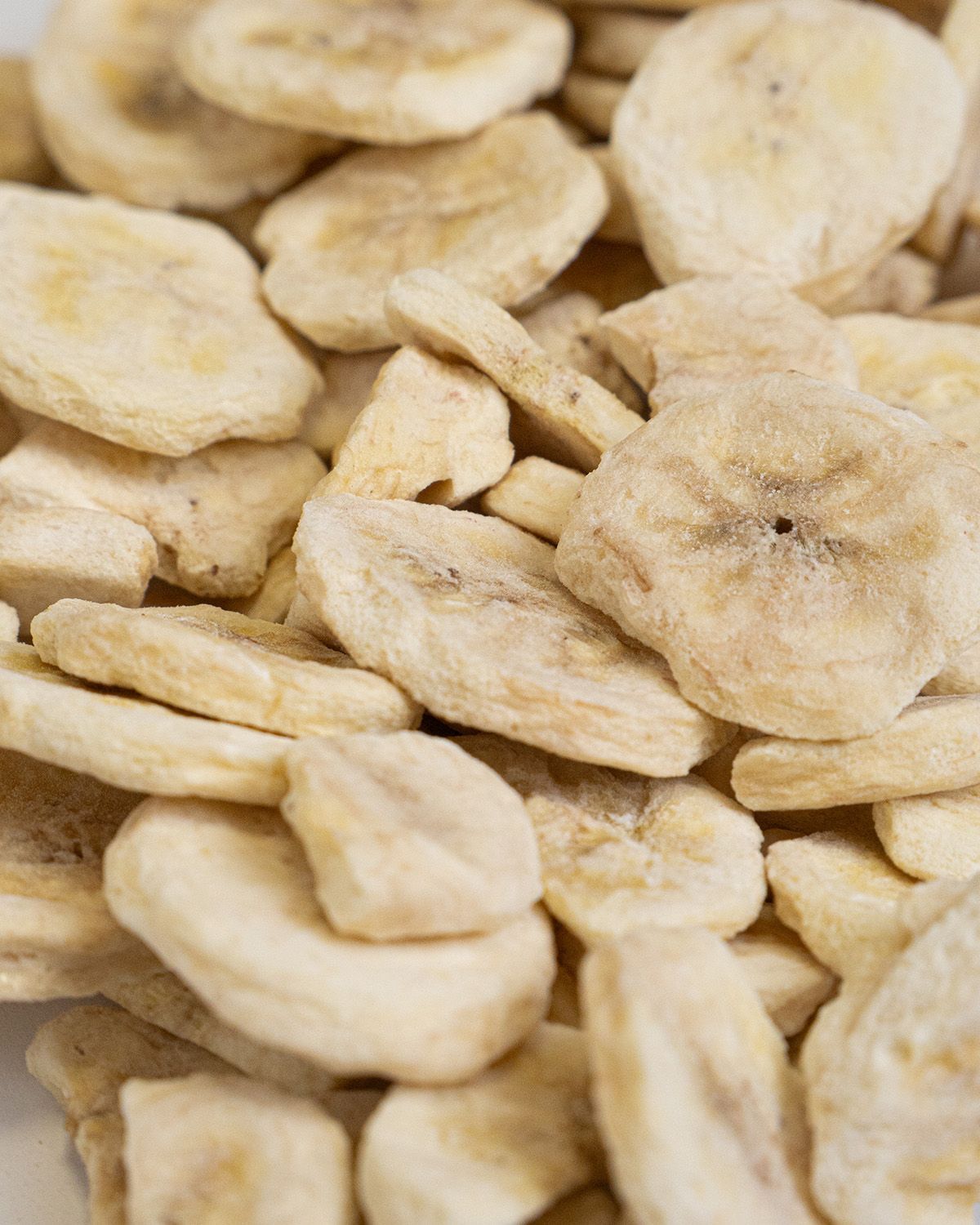 Nahaufnahme von gefriergetrockneten Bananenscheiben. Viele Scheiben liegen dicht beieinander.