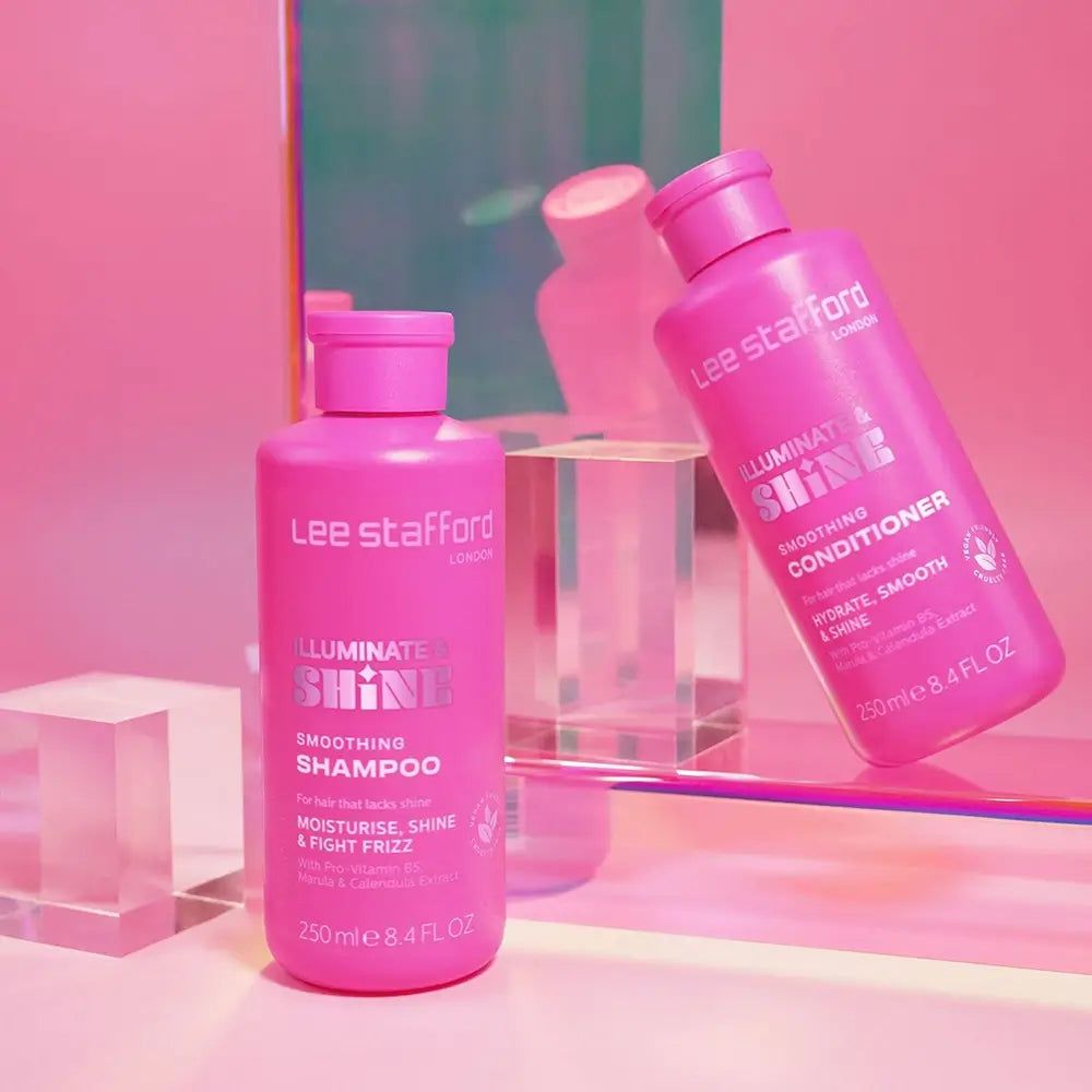 Zwei pinke Flaschen Lee Stafford Produkte, eine Spülung und ein Shampoo, auf einer Glasoberfläche.