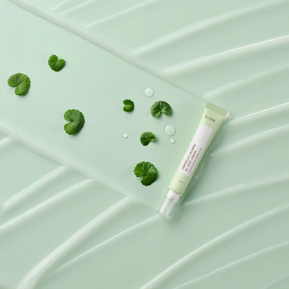 Grüne Tube auf grünem Untergrund mit Blättern und Wassertropfen. Aufschrift: iUNIK, Centella Calming AC Spot Cream.