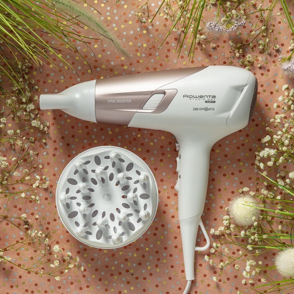 Weißer Haartrockner mit roségoldenen Akzenten und Diffusor. Marke Rowenta. Auf rosa Hintergrund mit Blumen.